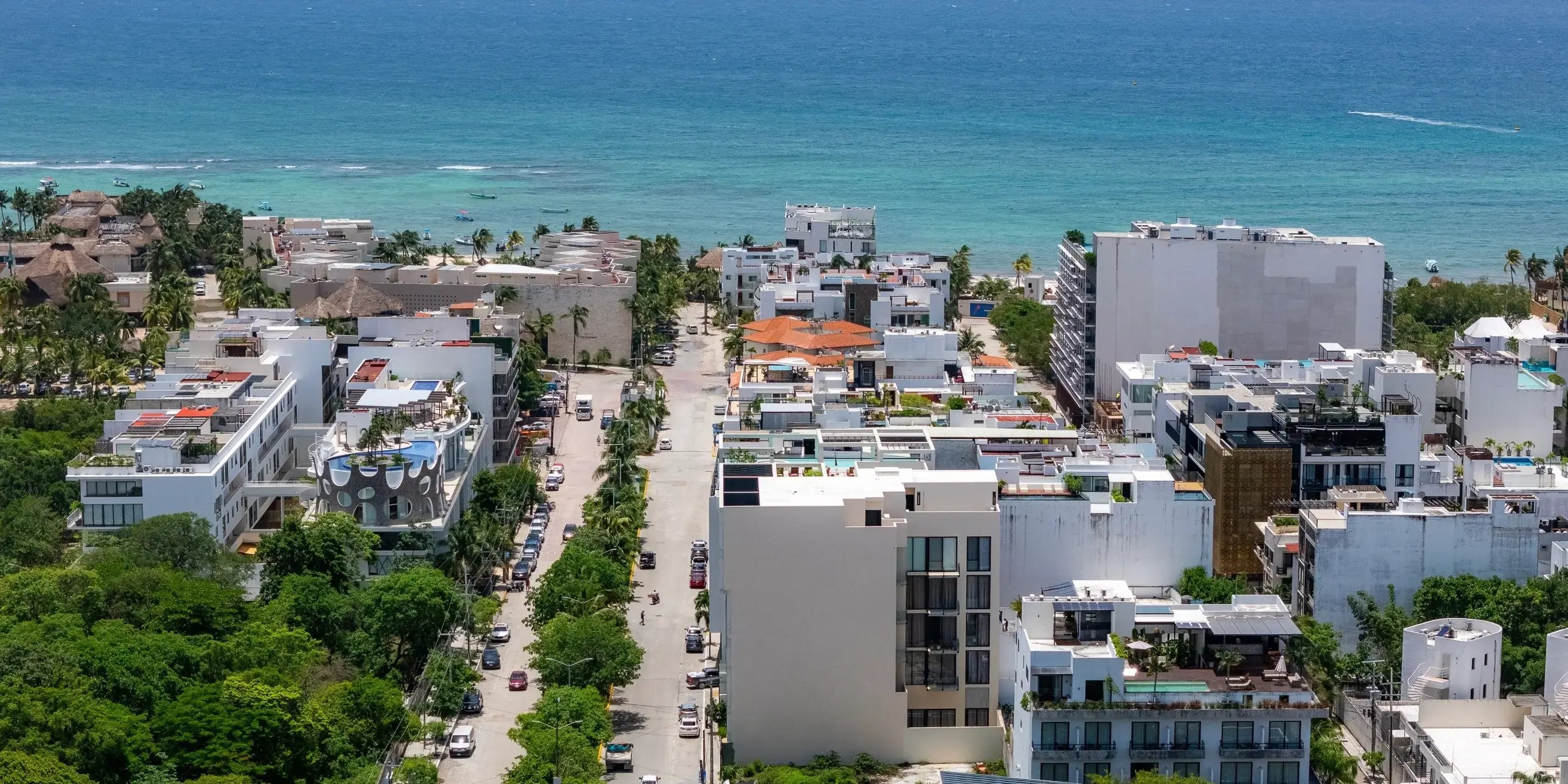 Vista aérea de las calles de Playa del Carmen, una de las mejores ciudades para vivir en México. Con áreas verdes y edificios blancos con piscina en la azotea y el mar Caribe azul en el fondo