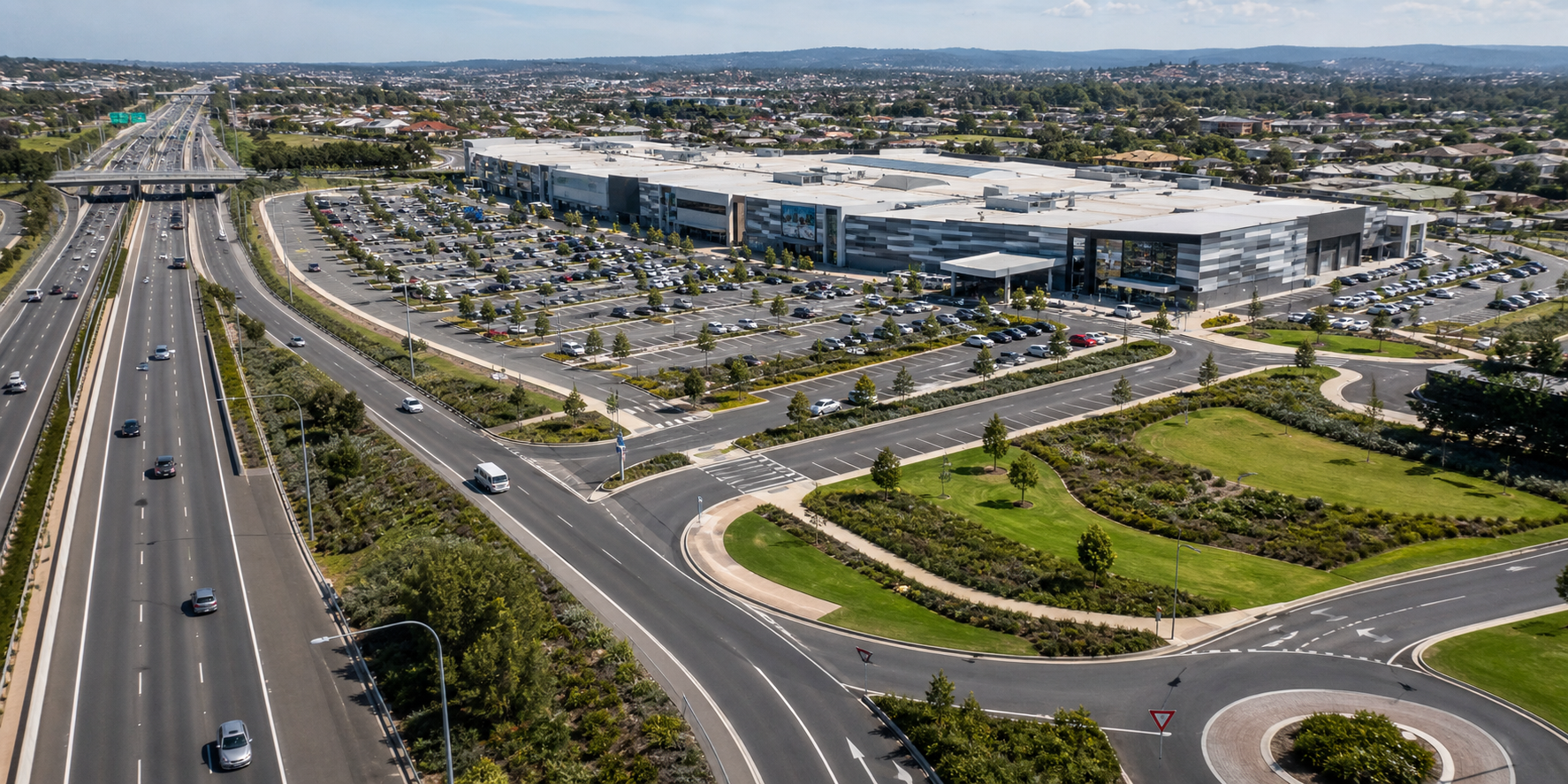 n moderno centro comercial ubicado junto a una autopista de varios carriles, con amplios accesos vehiculares, distribuidores viales, estacionamiento amplio, áreas verdes.