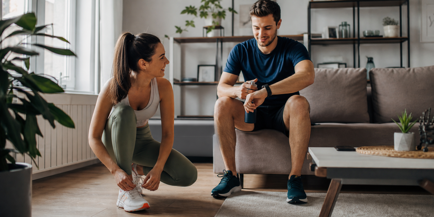 Una pareja en la sala de su casa preparándose para salir a correr y hacer ejercicio. Ambos llevan ropa deportiva moderna y tenis para correr.