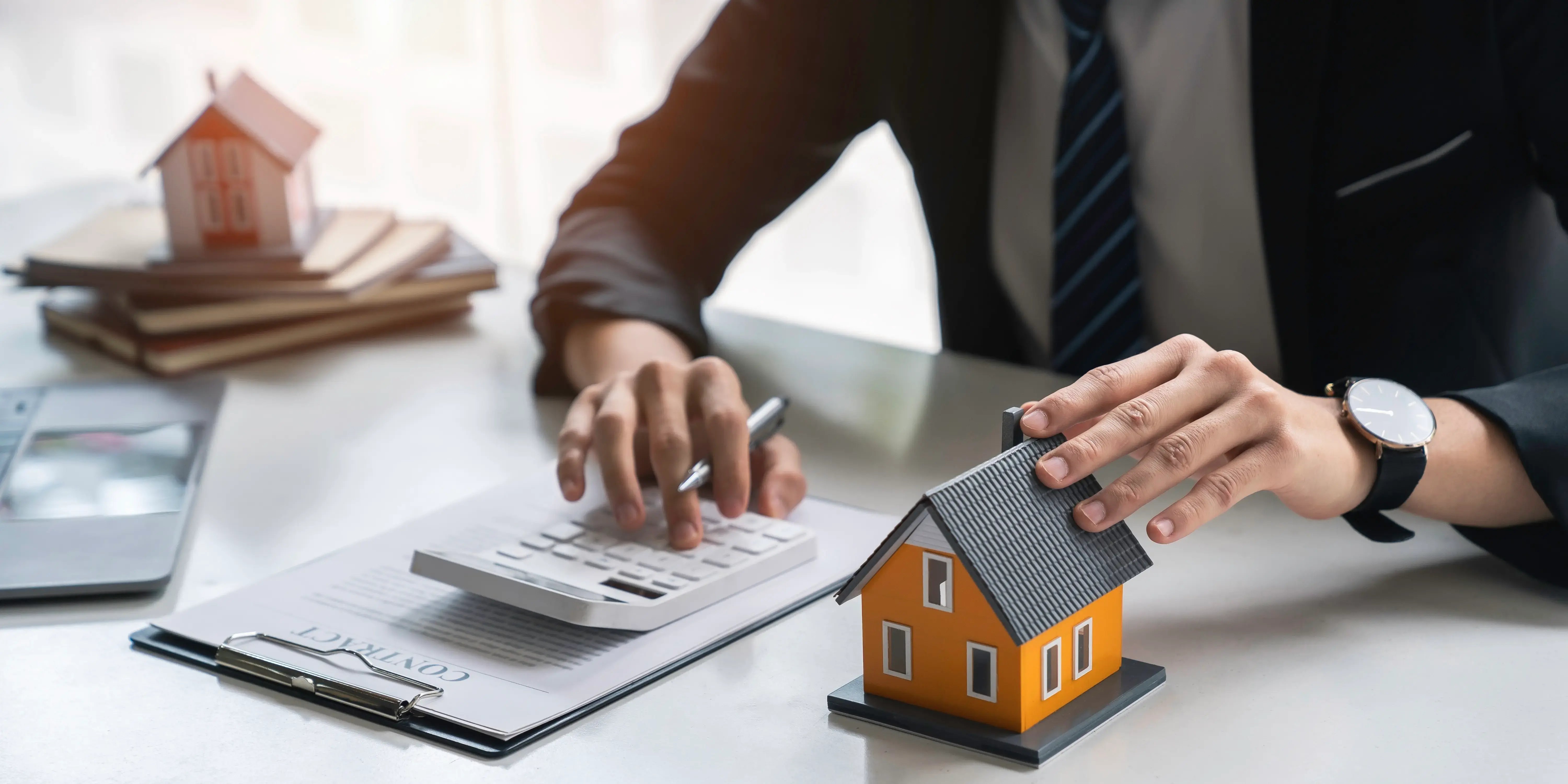 Agente inmobiliario con una calculadora y 2 casas de madera sobre el escritorio consultando con el cliente para la compra de una nueva casa con el crédito hipotecario linea 2 Infonavit