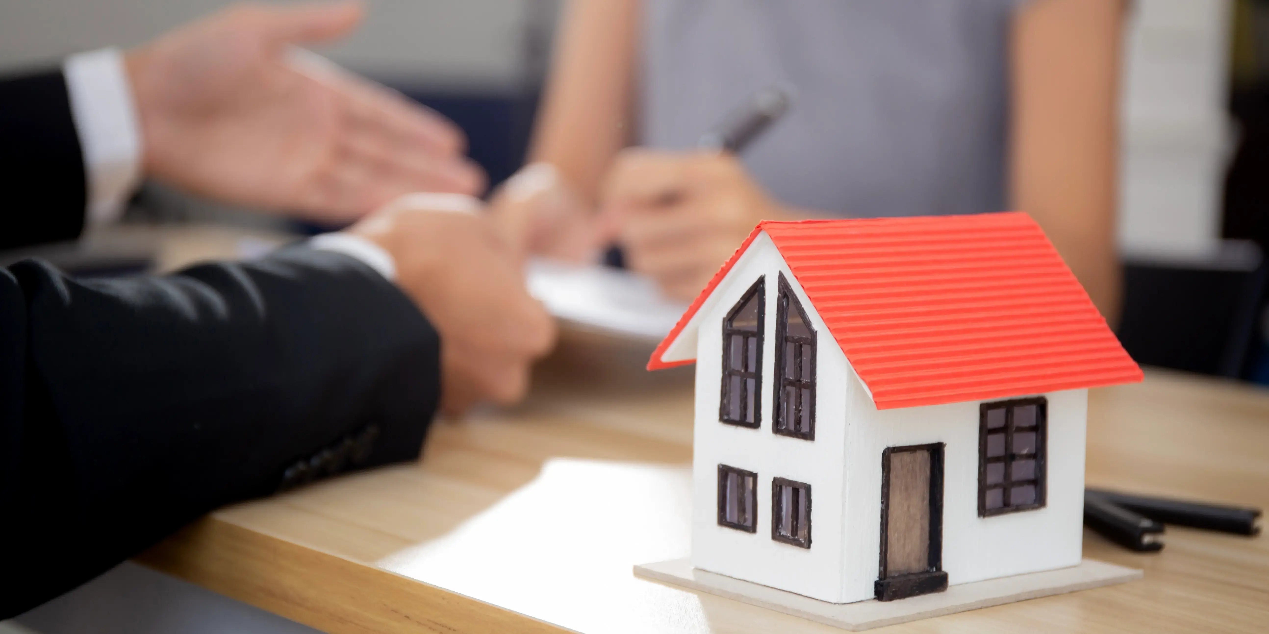 Agente inmobiliario explicando a cliente los requisitos para comprar casa por Infonavit y una casa modelo al frente