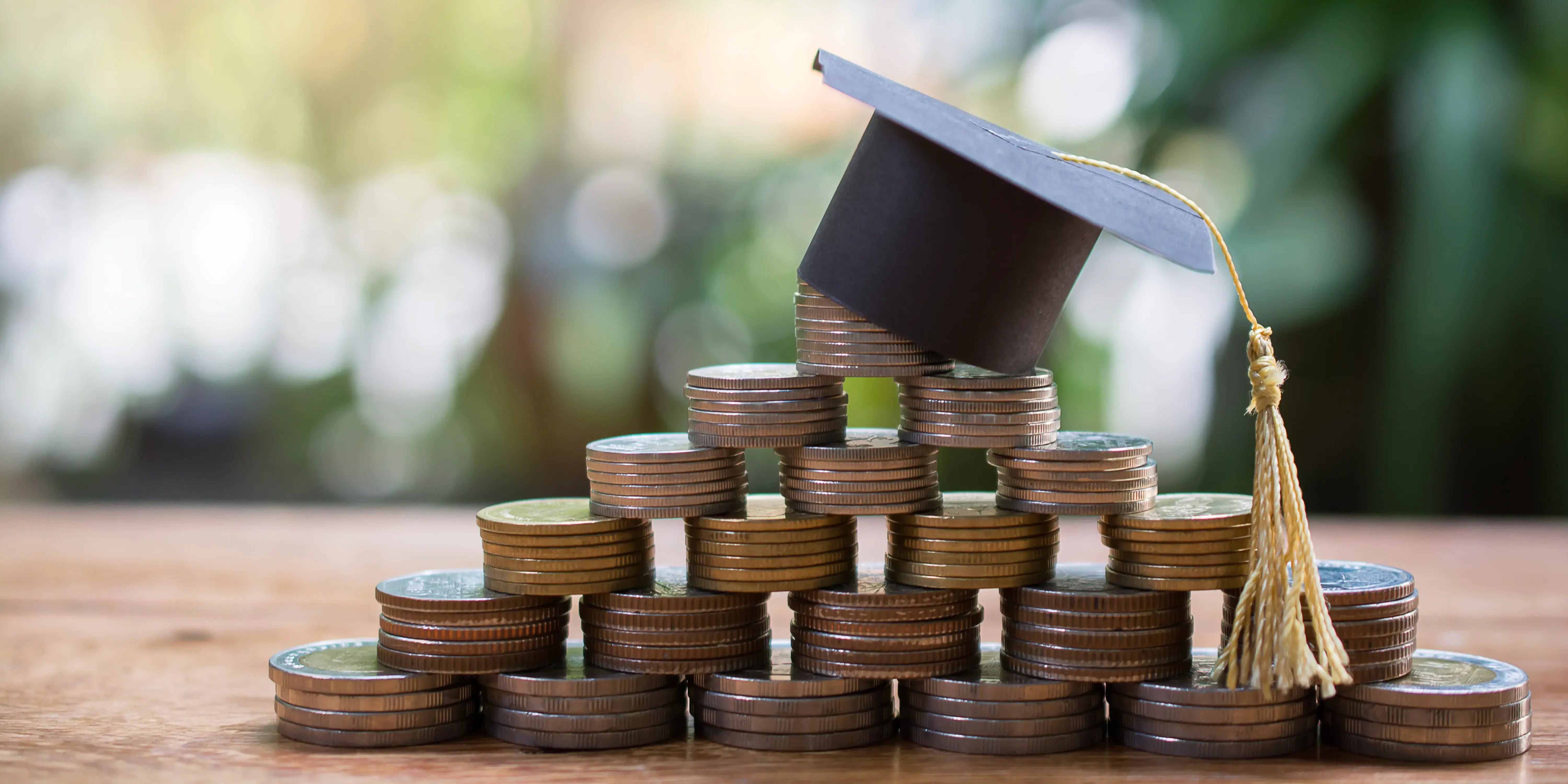 Birrete de graduación sobre torres de monedas por estudiar y mejorar tu establidad financiera