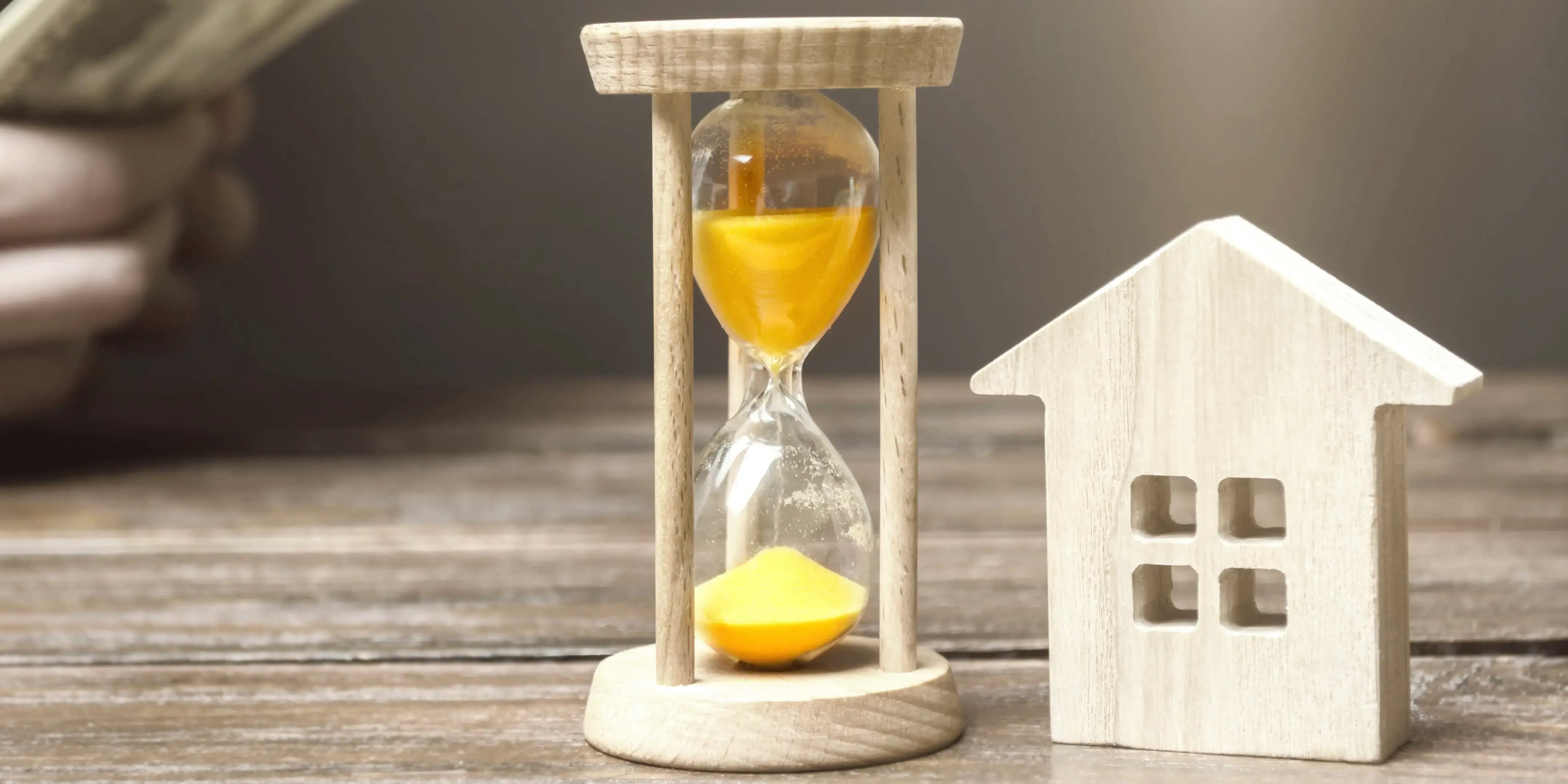 Casa de madera a un lado de un reloj de arena como ejemplo de inversión a corto plazo