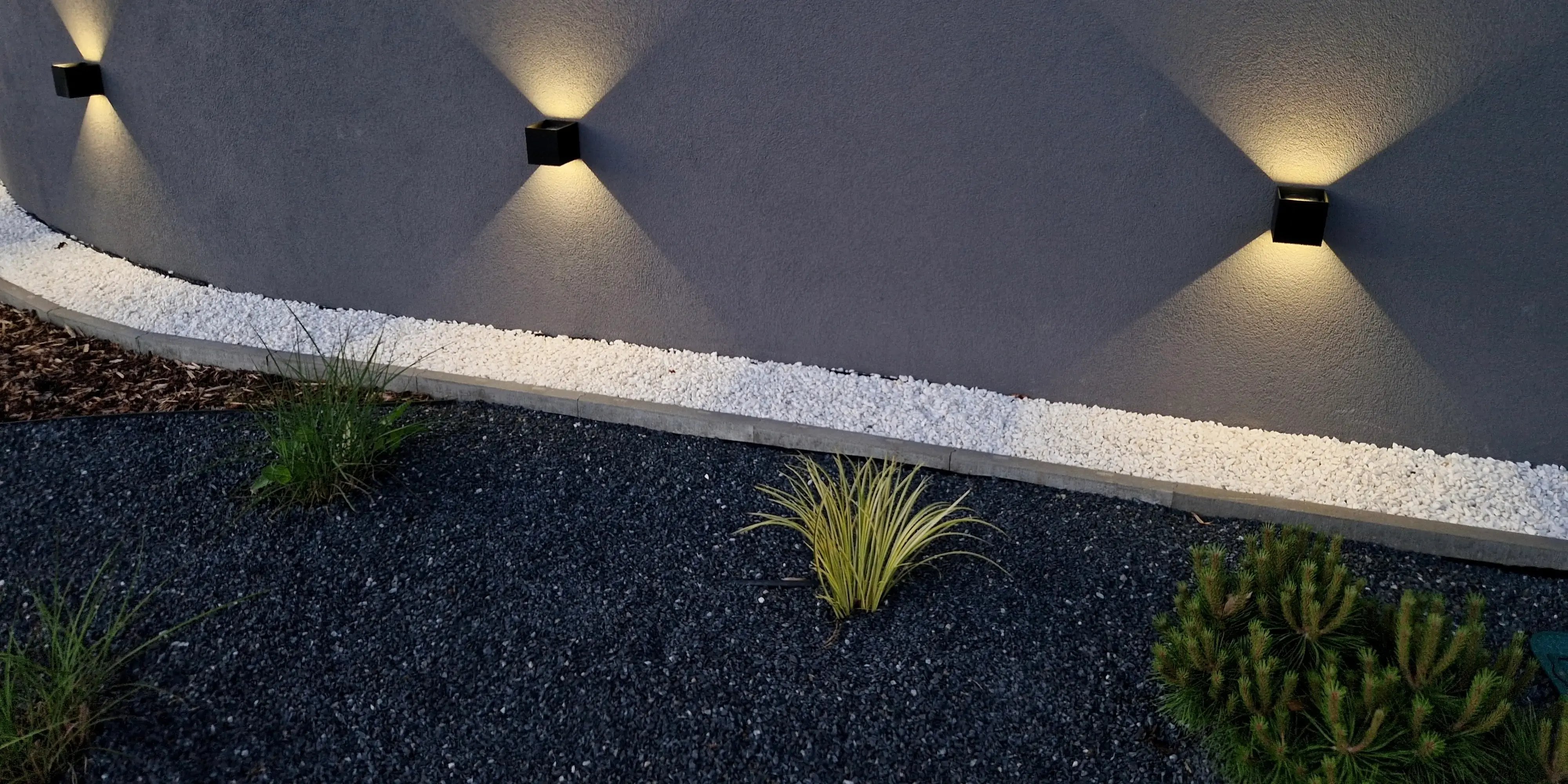 Fachada de casa moderna con focos empotrados iluminando la jardinera por la noche