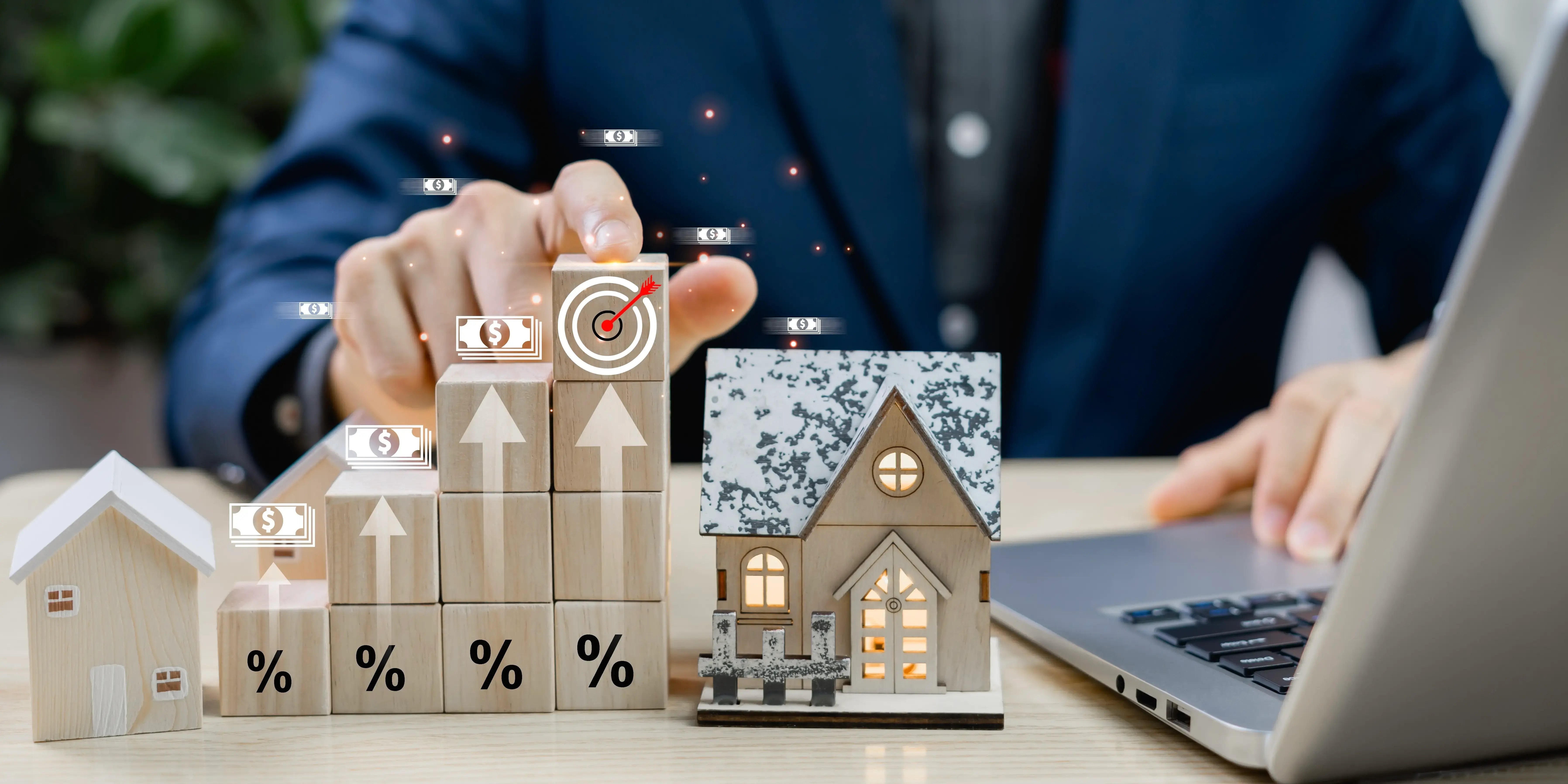 Hombre buscando en la computadora las opciones de inversión inmobiliaria en méxico, se muestran unos cubos de madera con el signo de porcentaje que van en aumento y dos casas de madera a los lados