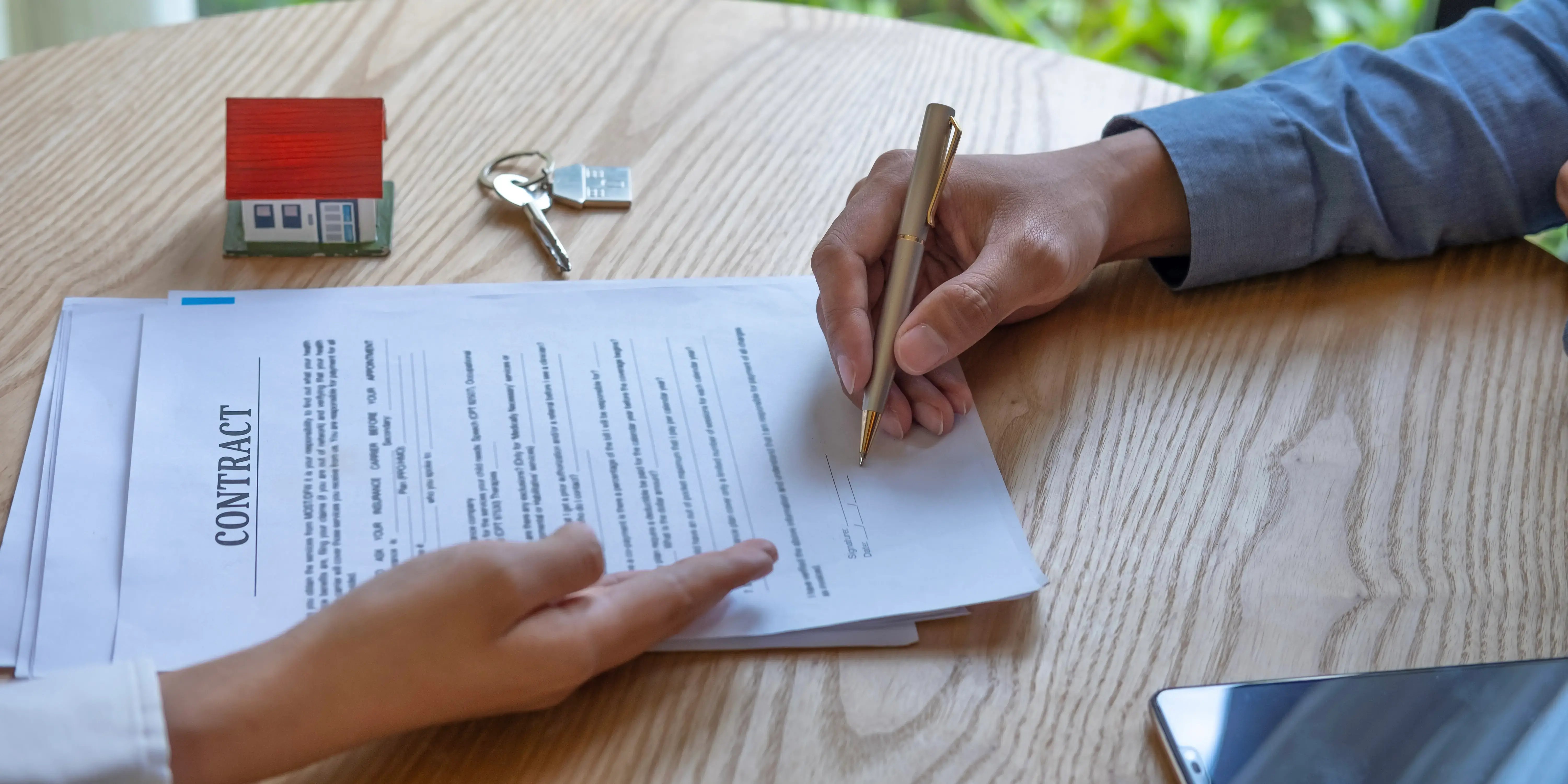 Hombre firmando un contrato de crédito hipotecario, en la mesa también hay unas llaves de una casa