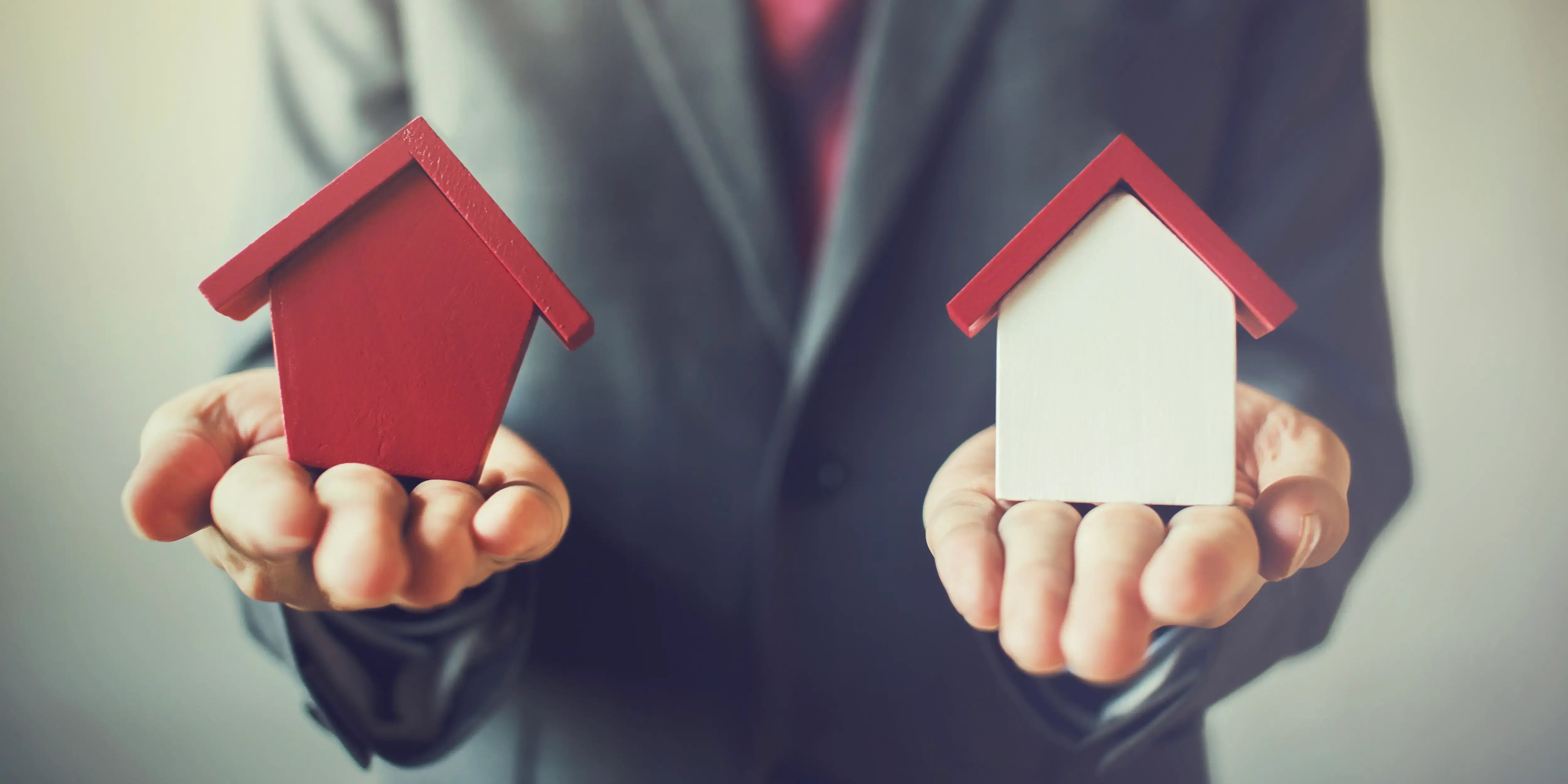 Hombre sosteniendo una casa roja y una casa blanca para decidir si va a rentar o revendarla por su plusvalía