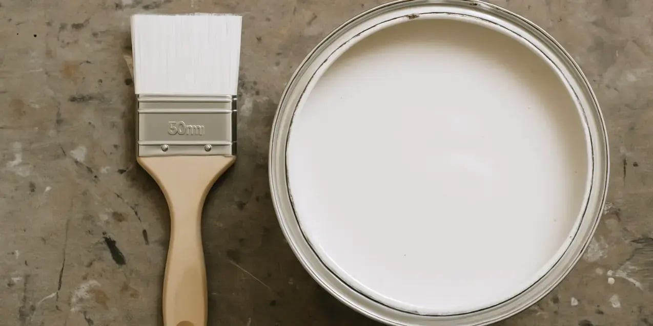 Imagen de una brocha y una pintura grande en color blanco sobre  una mesa de trabajo