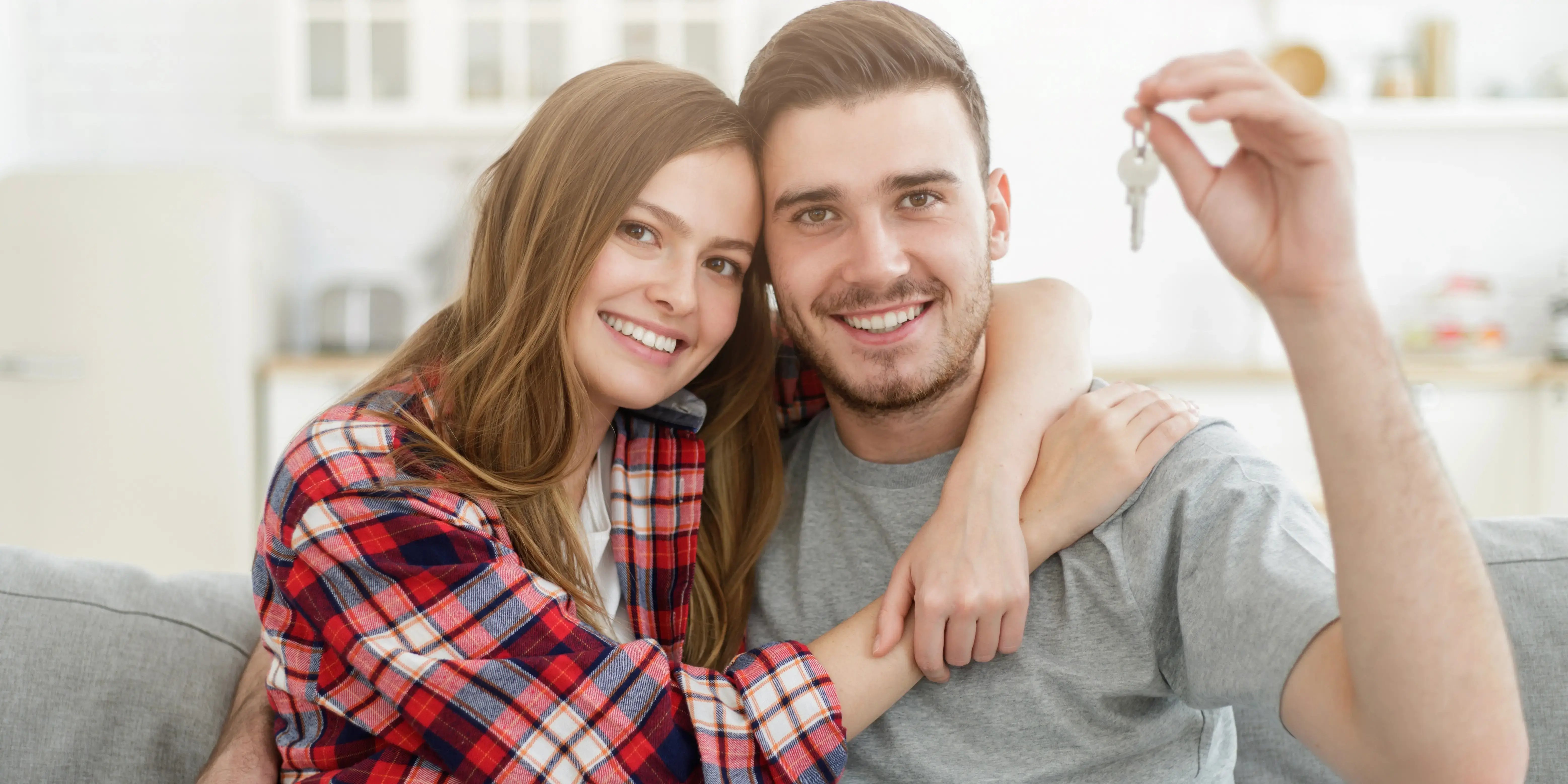Joven pareja feliz abrazándose, mostrando las llaves de la casa nueva que compró con crédito FOVISSSTE
