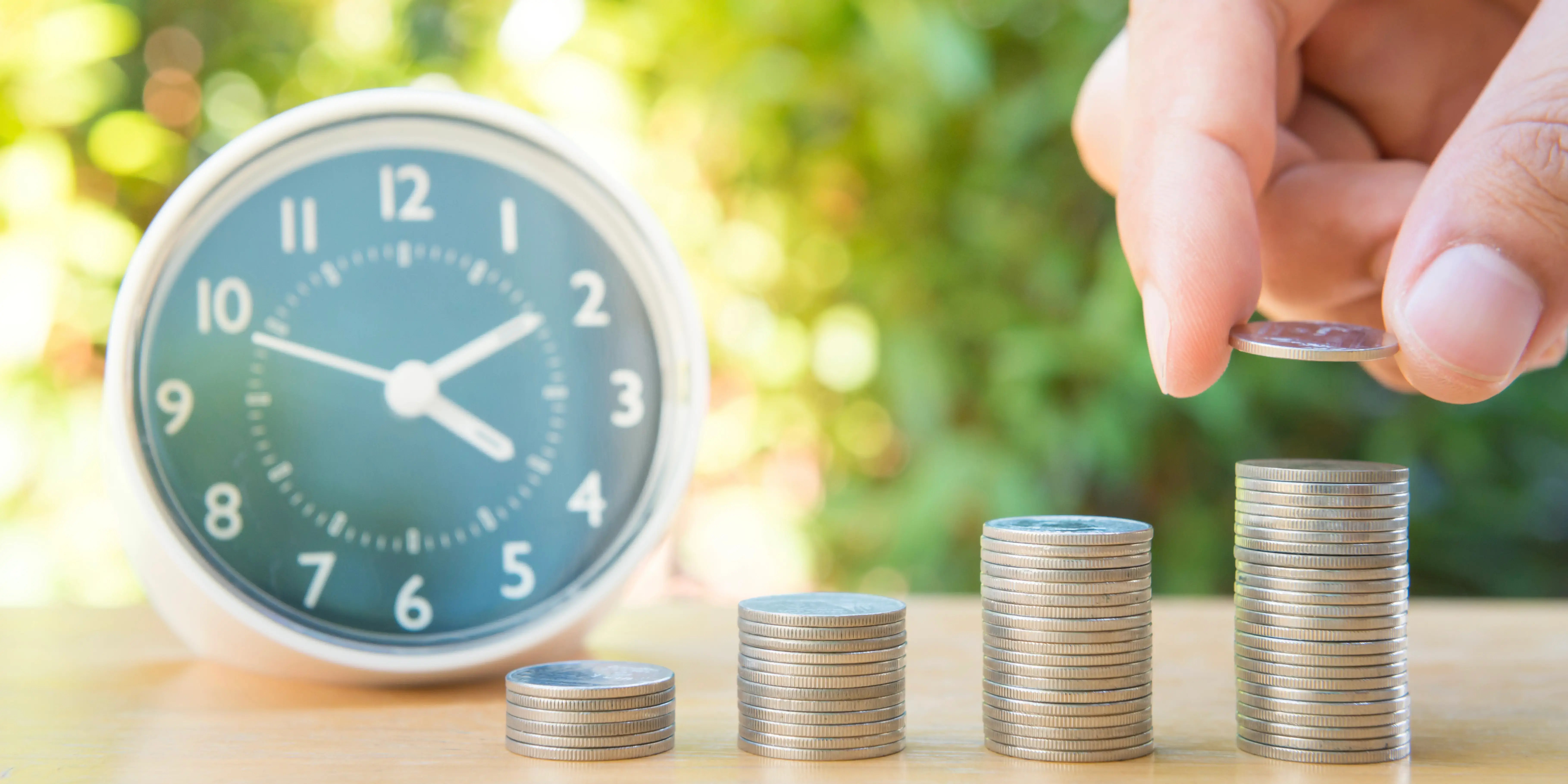 Mano colocando torres de monedas a un lado de un reloj como ejemplo de inversiones a largo plazo
