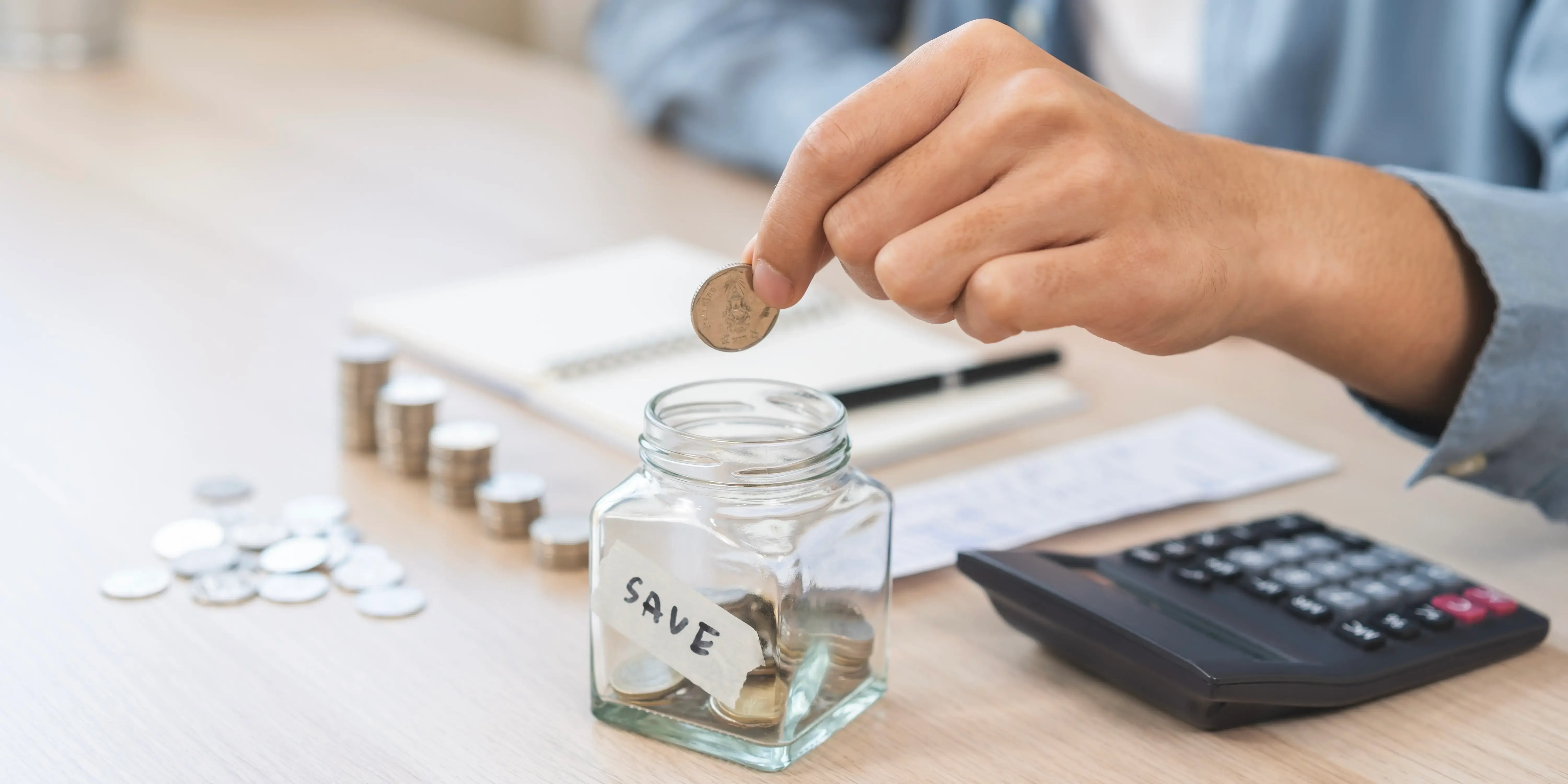 Mano de joven poniendo moneda en tarro para ahorrar y buscando los distintos tipos de cuentas de ahorro