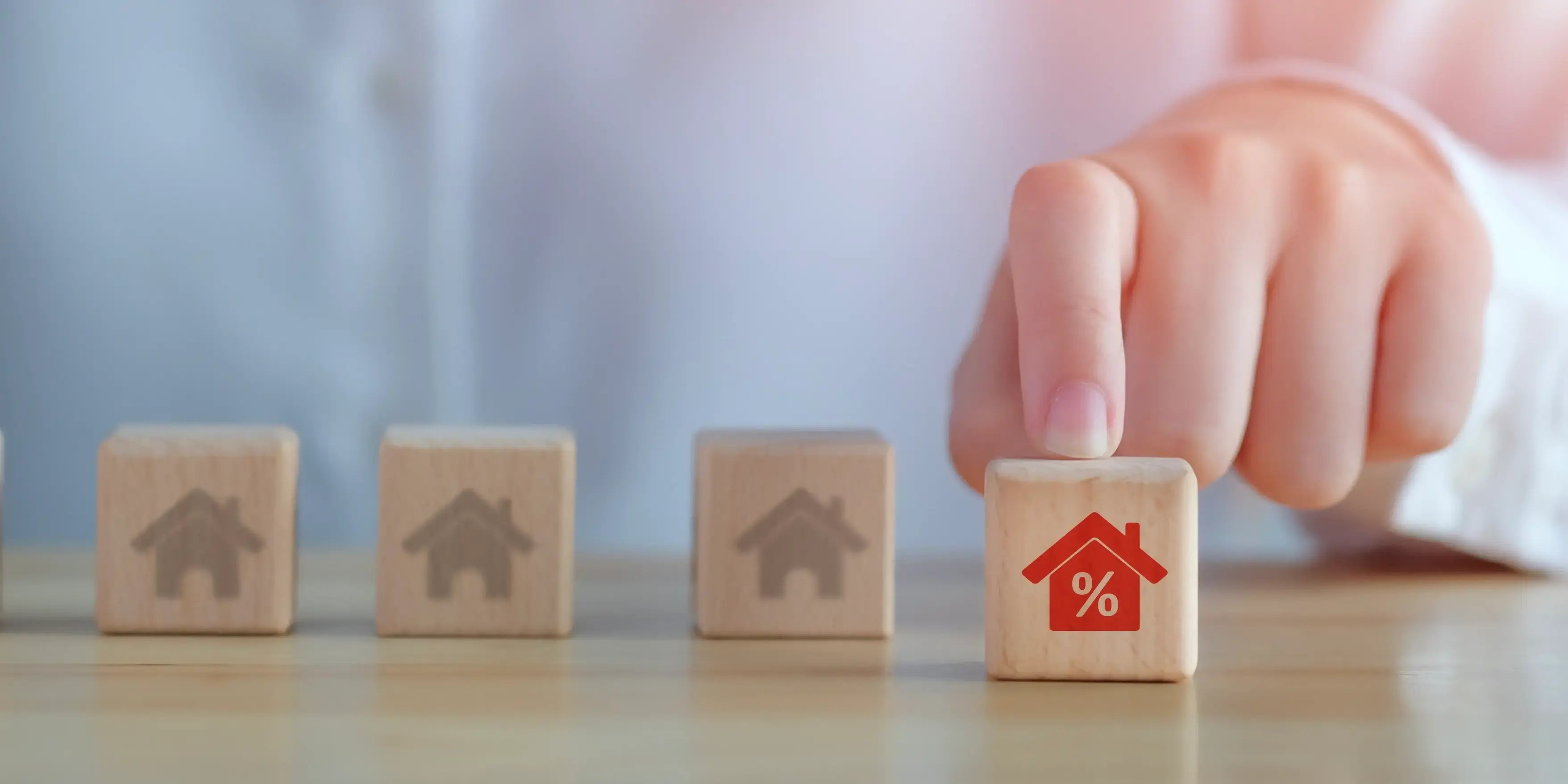 Mano señalando cubo de madera con la imagen de una casa de color rojo por los descuentos inmobiliarios