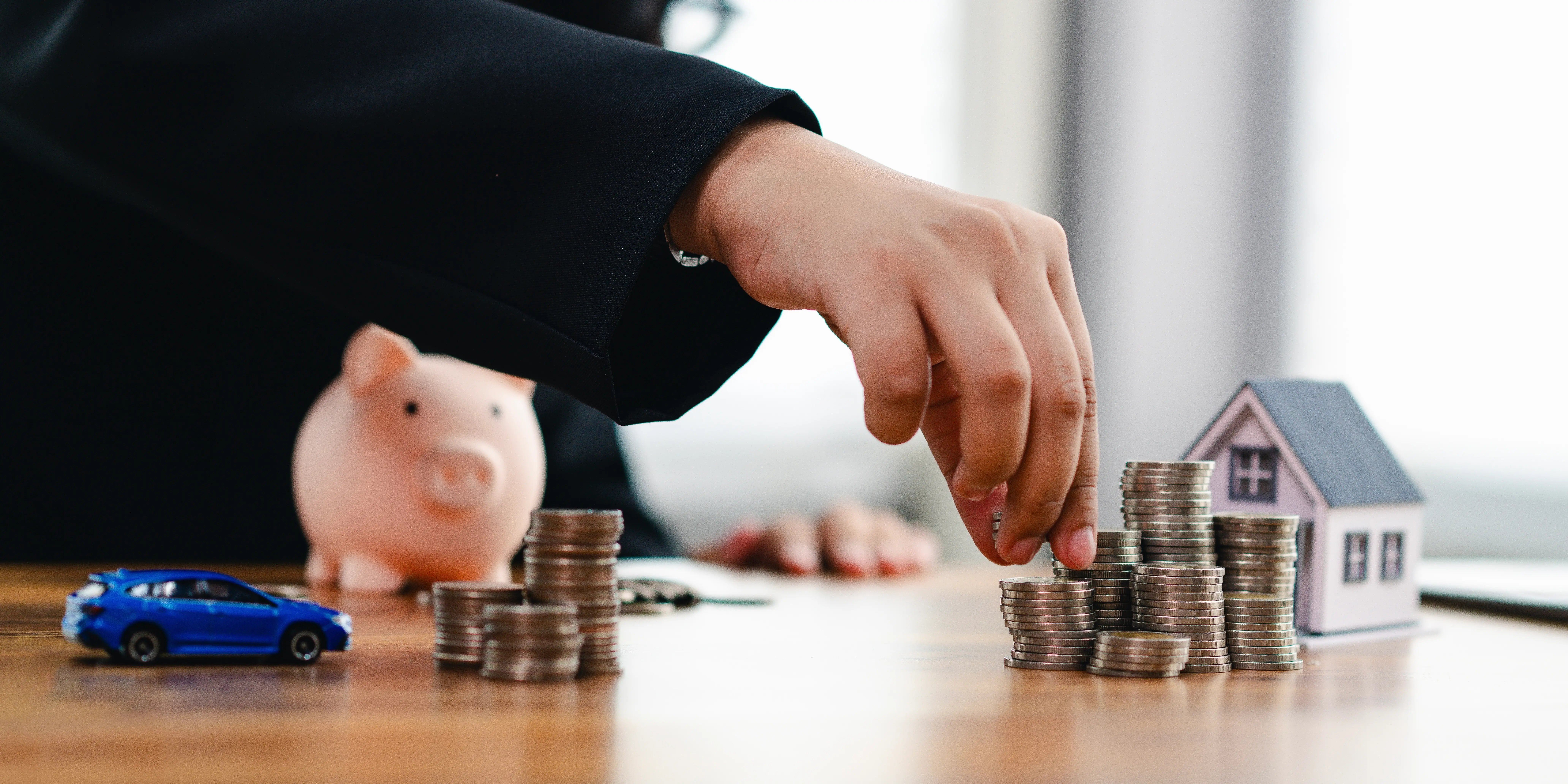 Mujer aplilando torres de monedas sobre una mesa para alcanzar sus metas de planeación financiera y comprar una casa