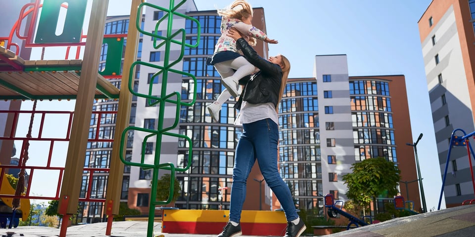Mujer cargando a su hija en las juegos infantiles al decidir comprar casa o departamento con amenidades