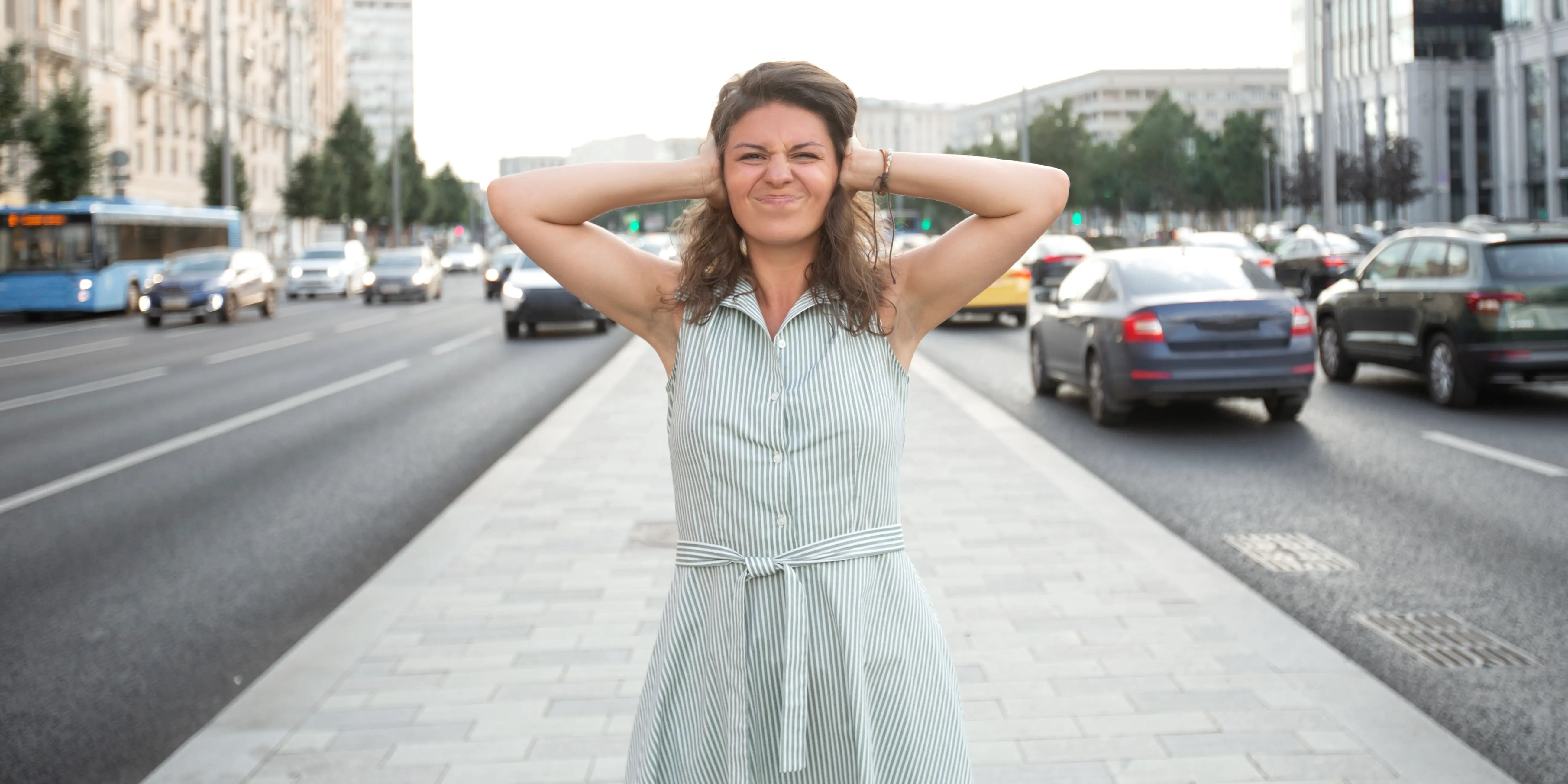 Mujer en medio de la calle frunce el ceño y se cubre las orejas con las manos por el ruido de vivir cerca del transporte público