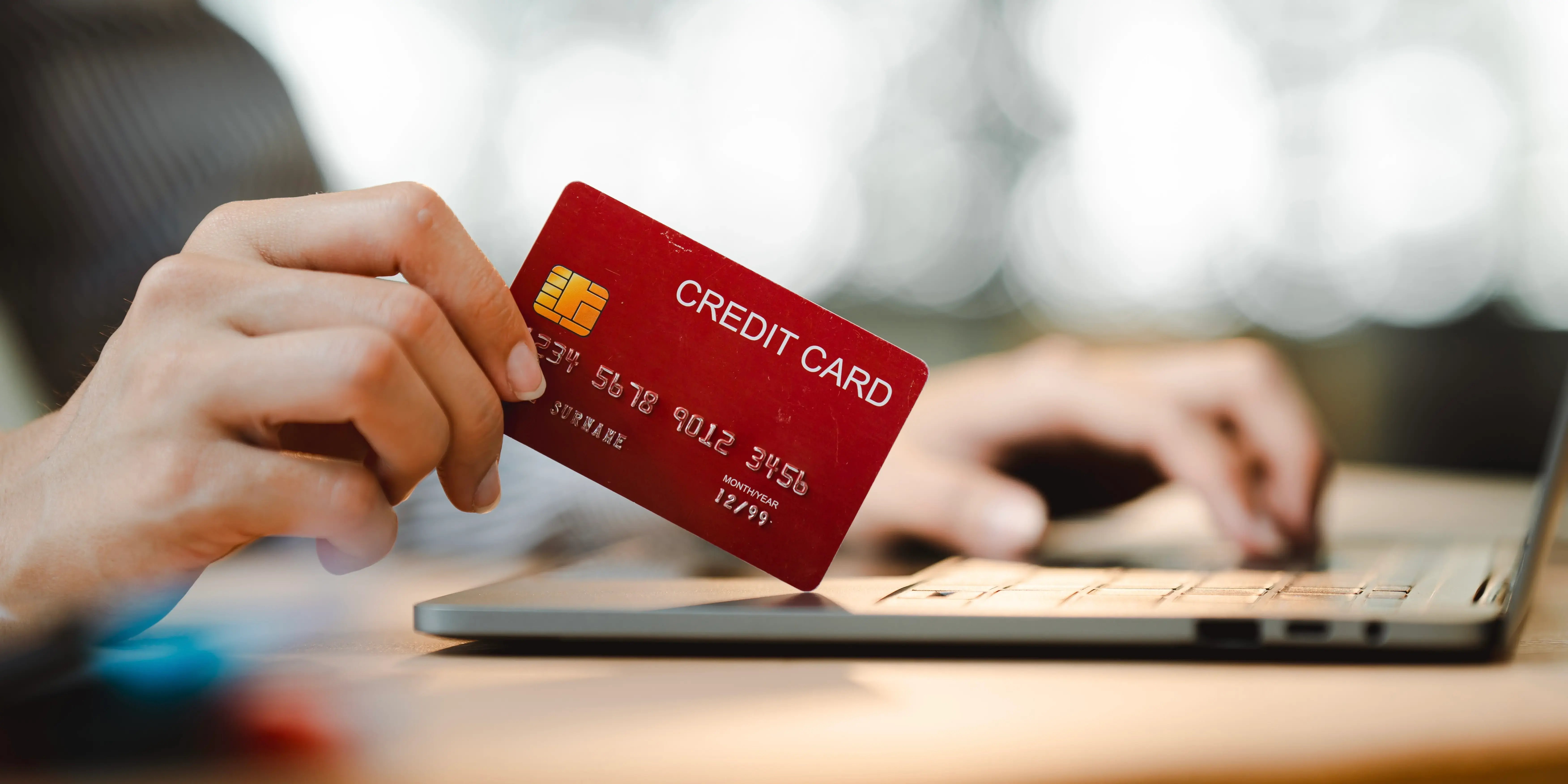 Mujer sosteniendo una tarjeta de crédito y utilizando una computadora para conocer los beneficios y contras de un crédito bancario