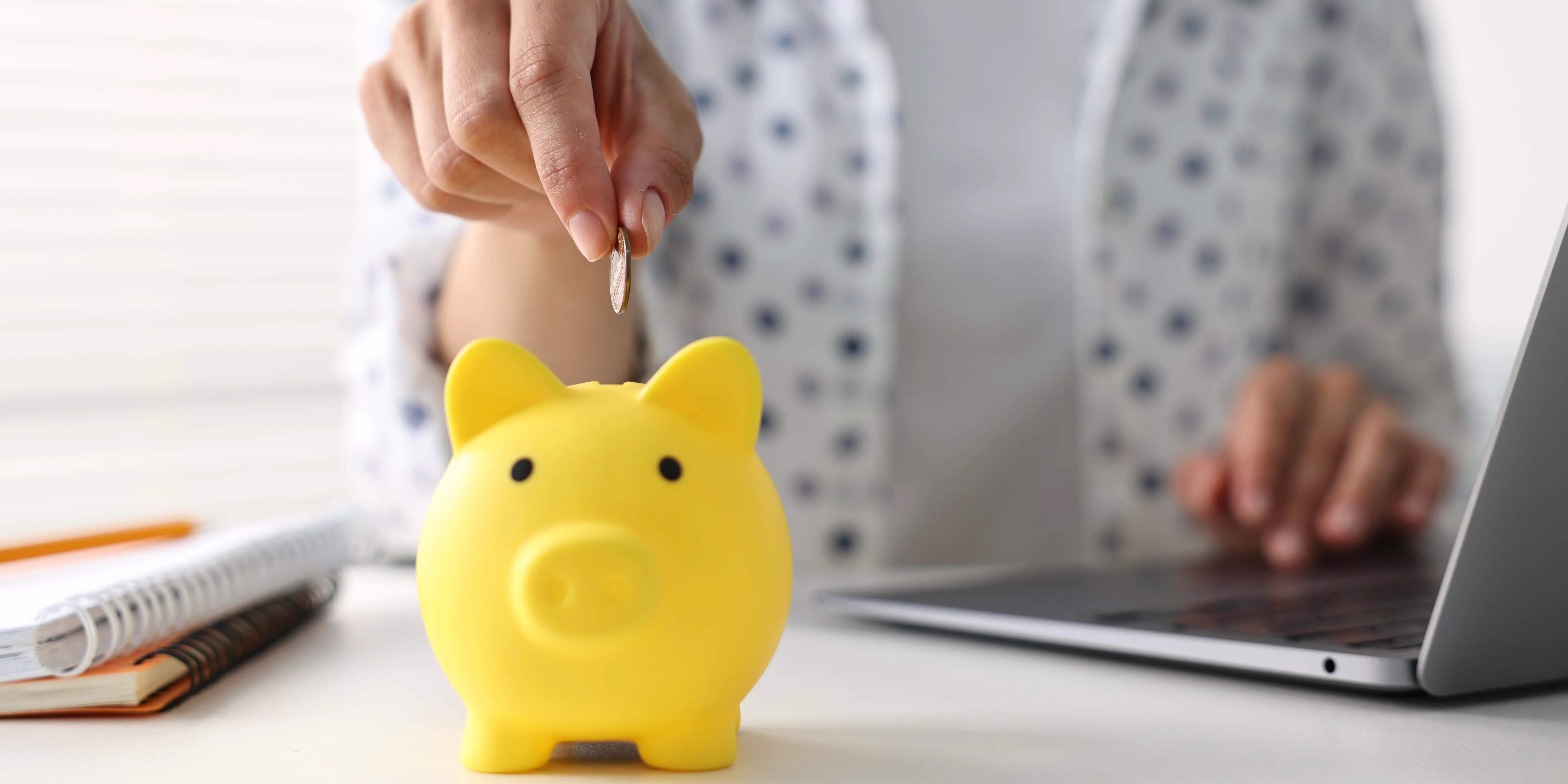 Mujer usando una computadora y metiendo unas monedas a una alcancía para maximizar sus ahorros