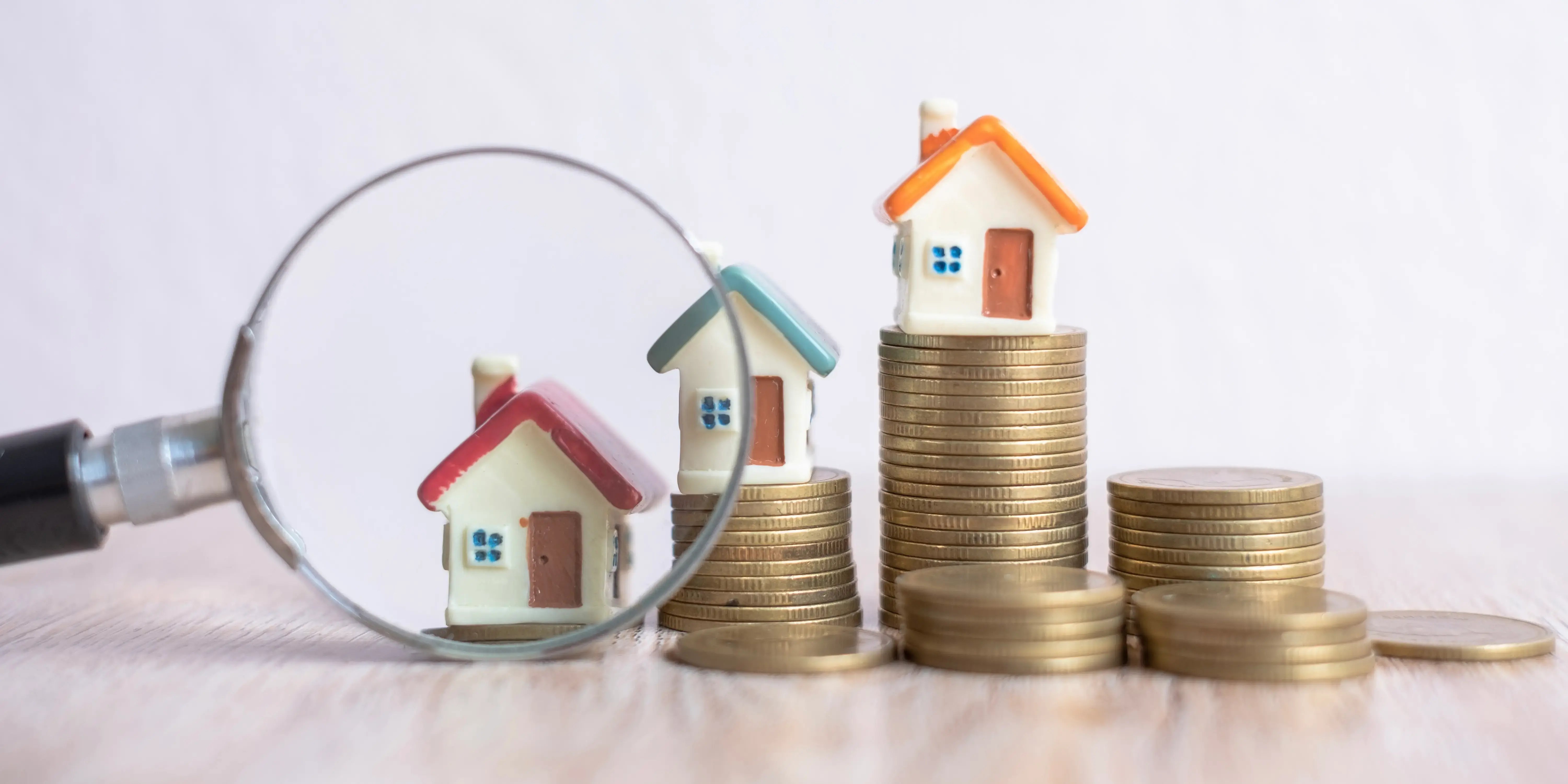 Observando con una lupa unas miniatura de casa que se encuentran sobre unas torres moneda para diferenciar los tipos de plusvalía