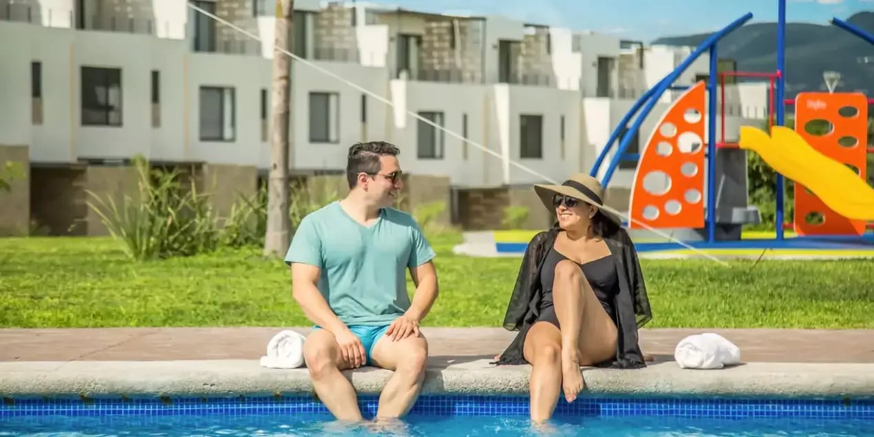 Pareja sentada a la orilla de la alberca en Santa Fe Lifestyle