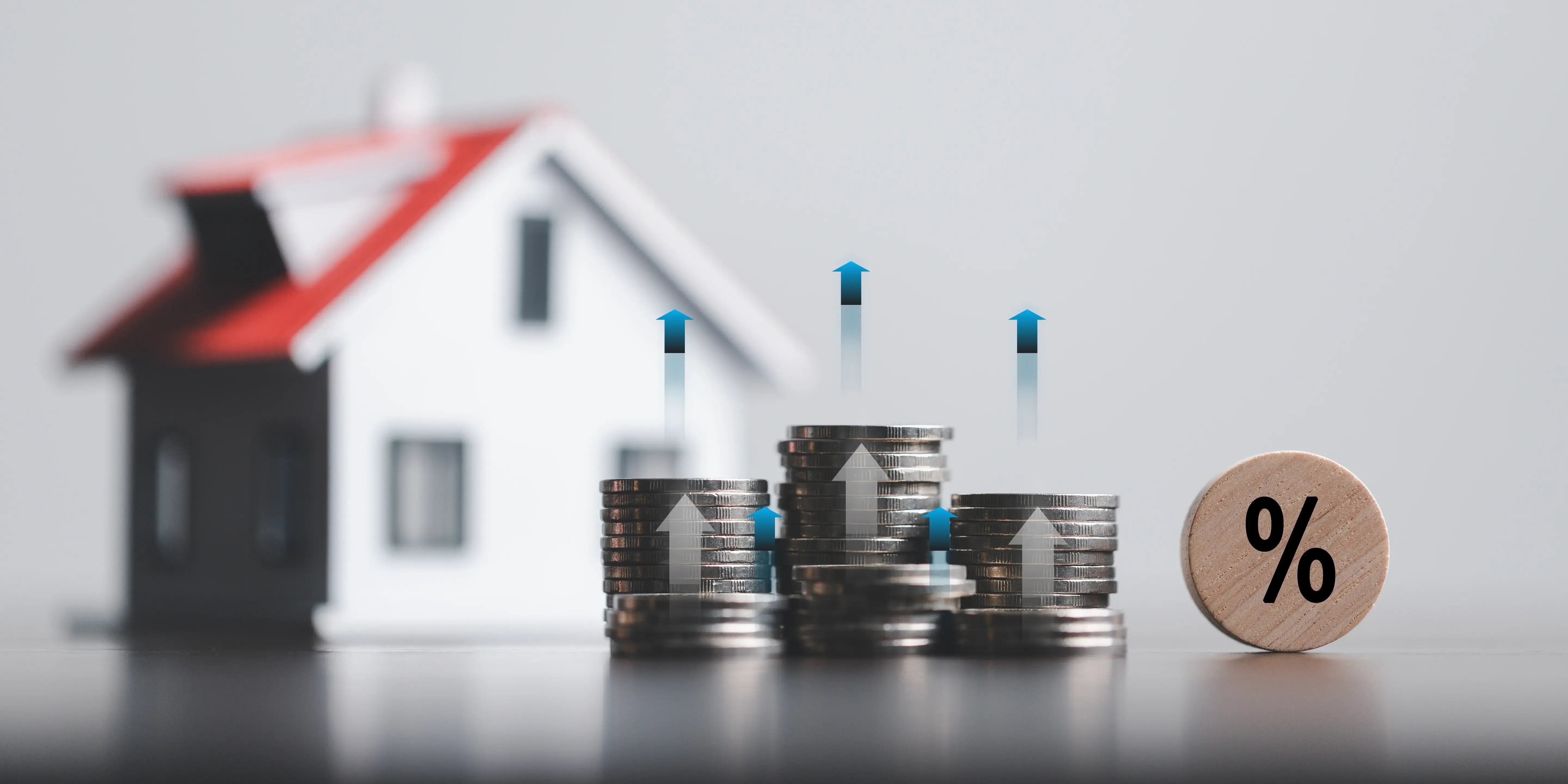 Pilas de monedas y maqueta de casa con símbolo porcentual de tasa de interés por garantía hipotecaria