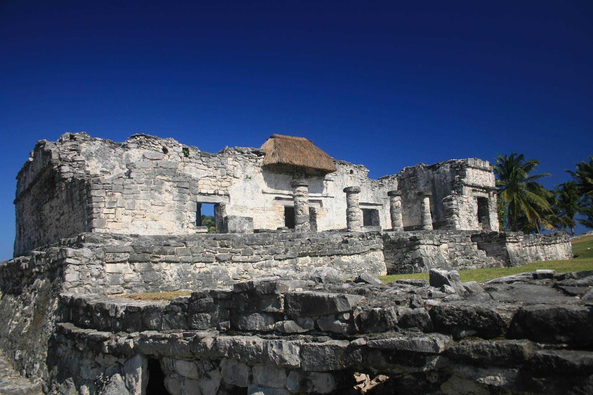 Ruinas de Tulum en la Riviera Maya con un cielo azul marino, dos palmas a la derecha. Es una zona arqueológica. 