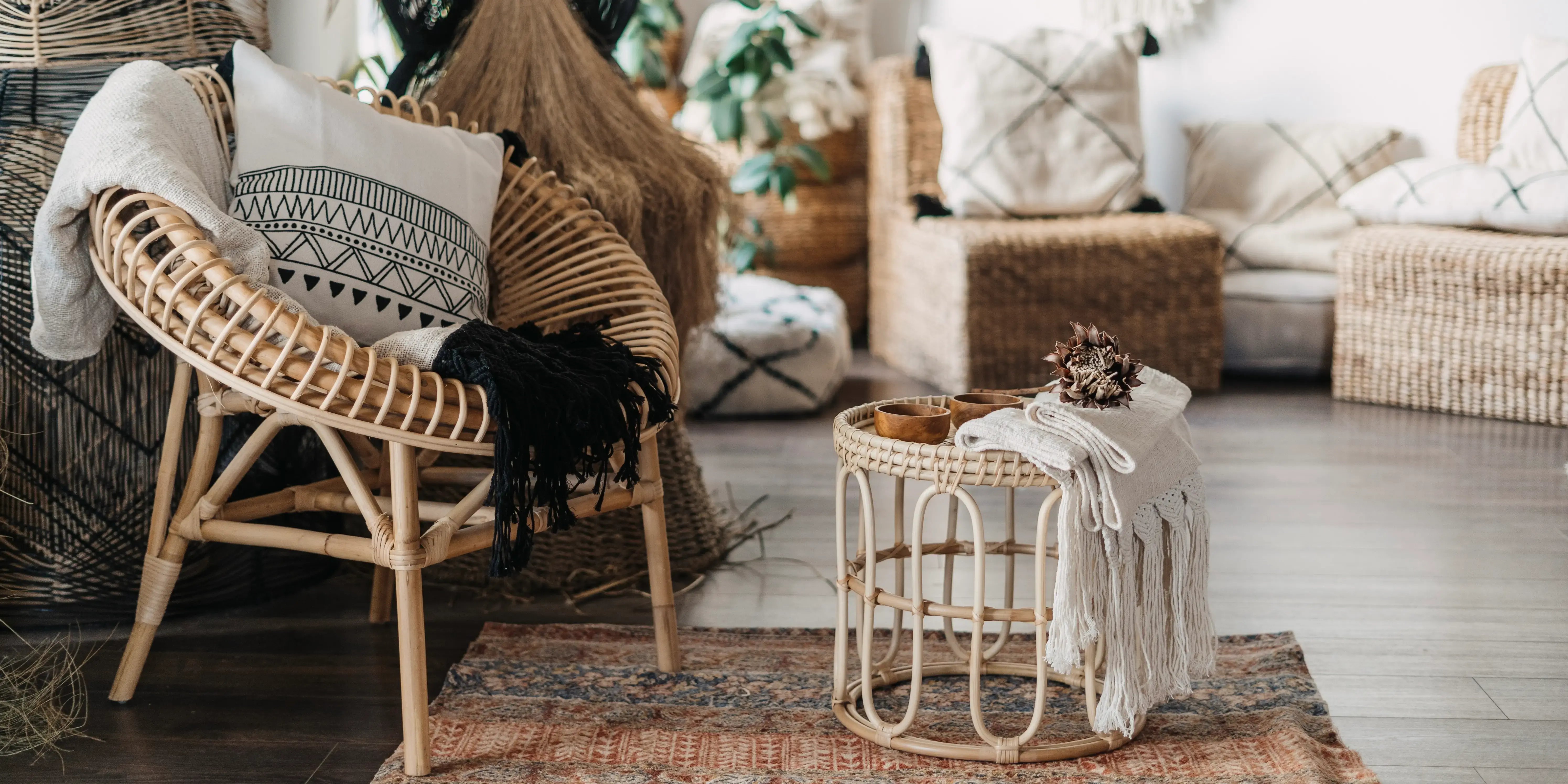 Sala con diseño de interiores estilo Boho Chic con mobiliario de mimbre, sillón con cojines ymesa baja de bambú