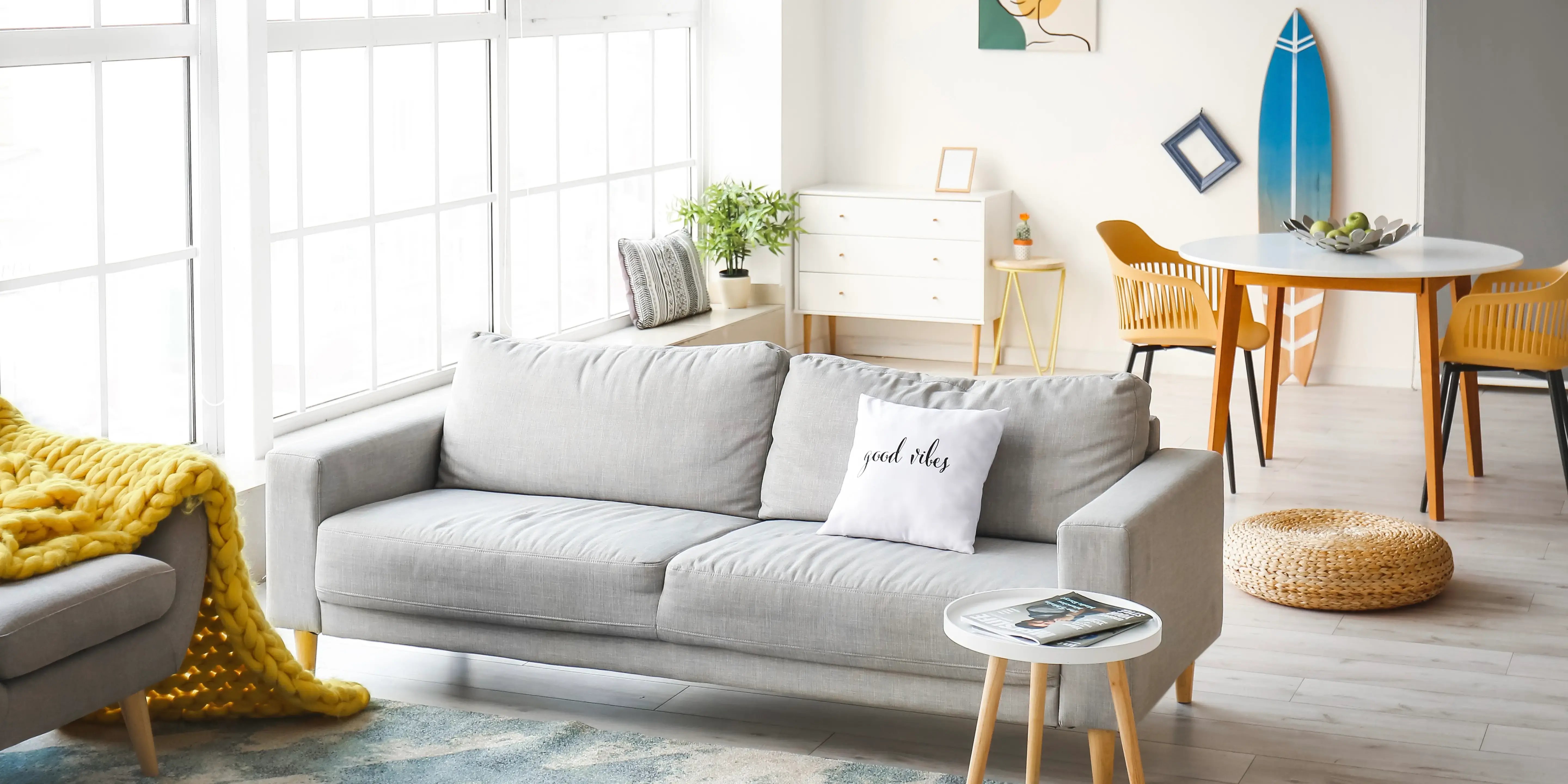Sala con diseño de interiores estilo costero con puertas corredizas, muebles de mibre y sillón de lino y al fondo una tabla de surf