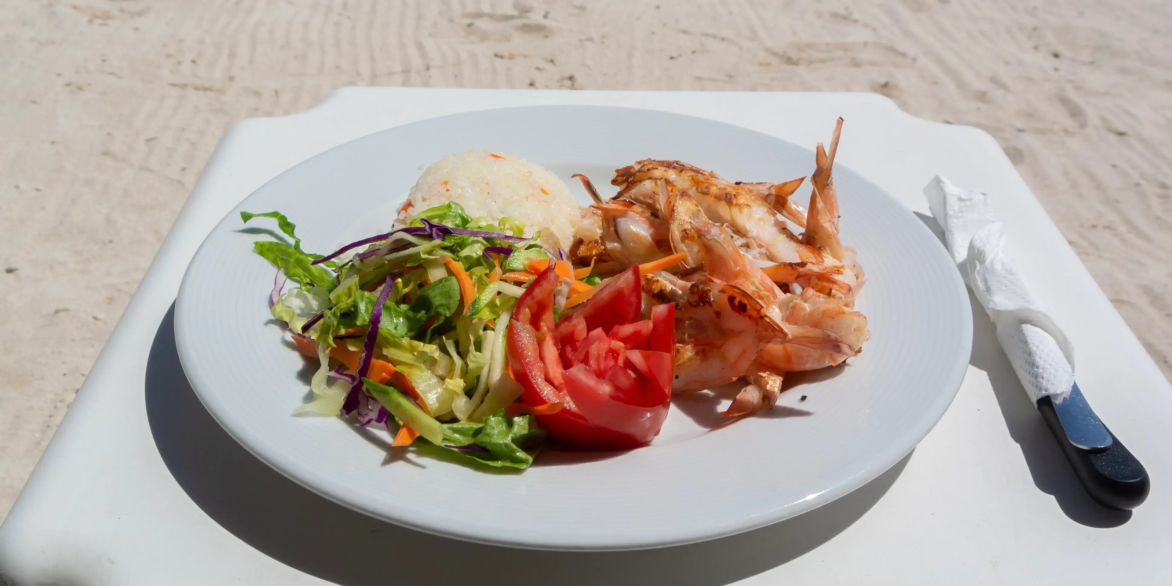 Un plato blanco con gambas a la parrilla en un restaurante de beach club