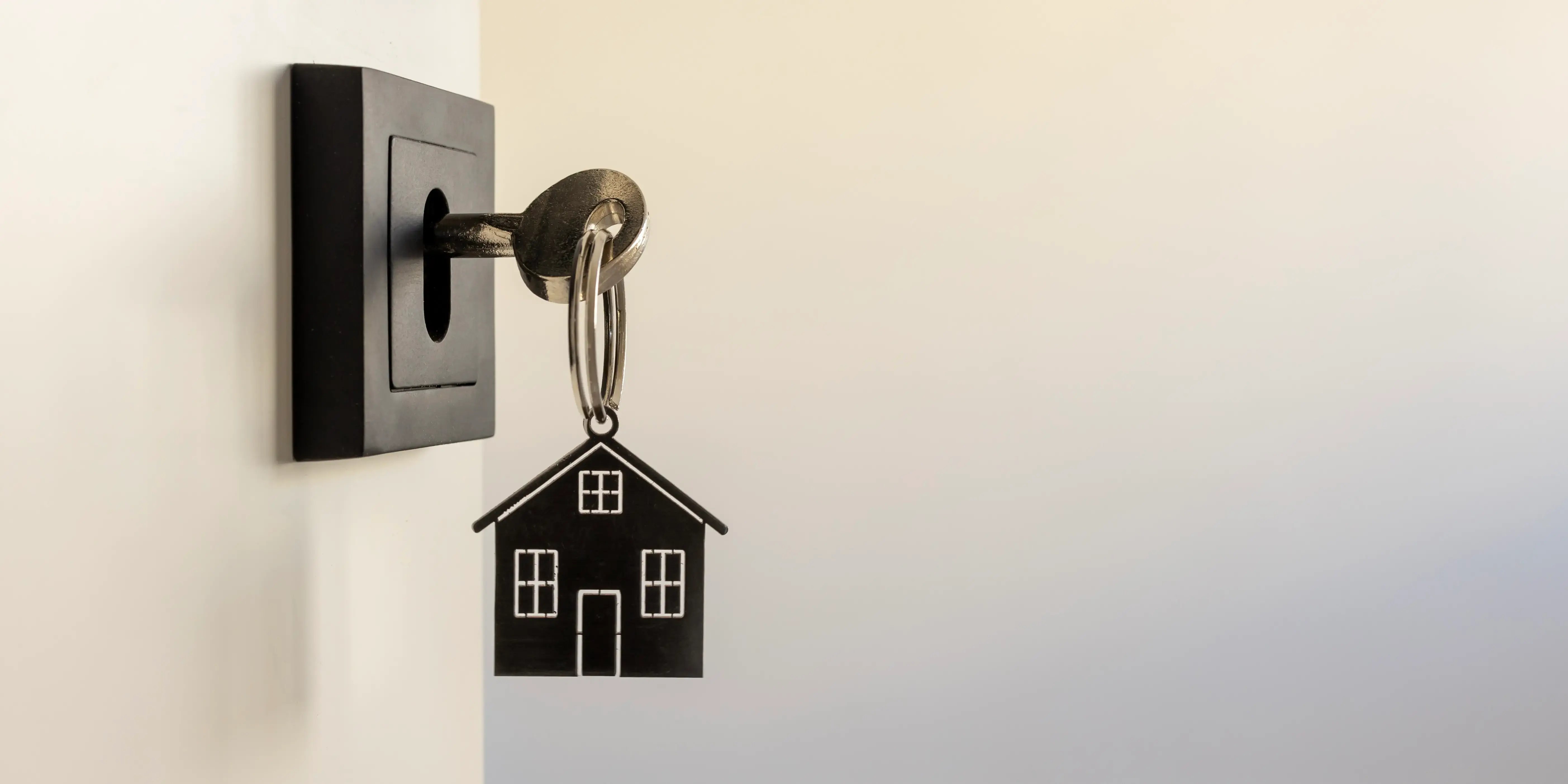 Una llave en una cerradura de puerta moderna con un llavero en forma de casa, que simboliza invertir en una casa nueva