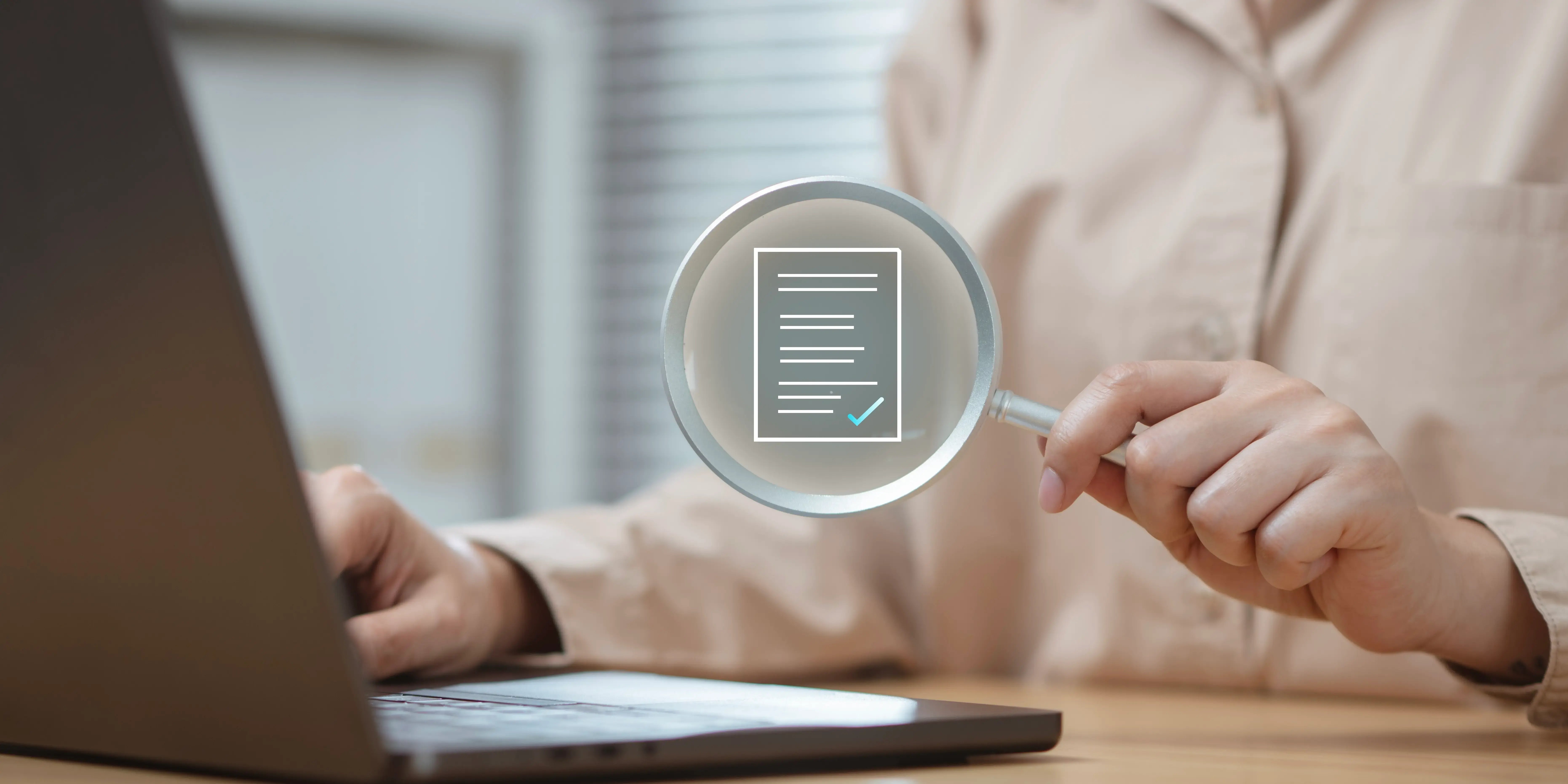 Una mujer sosteniendo una lupa y mirando en su computadora los documetos que necesita para comprar casa por Infonavit