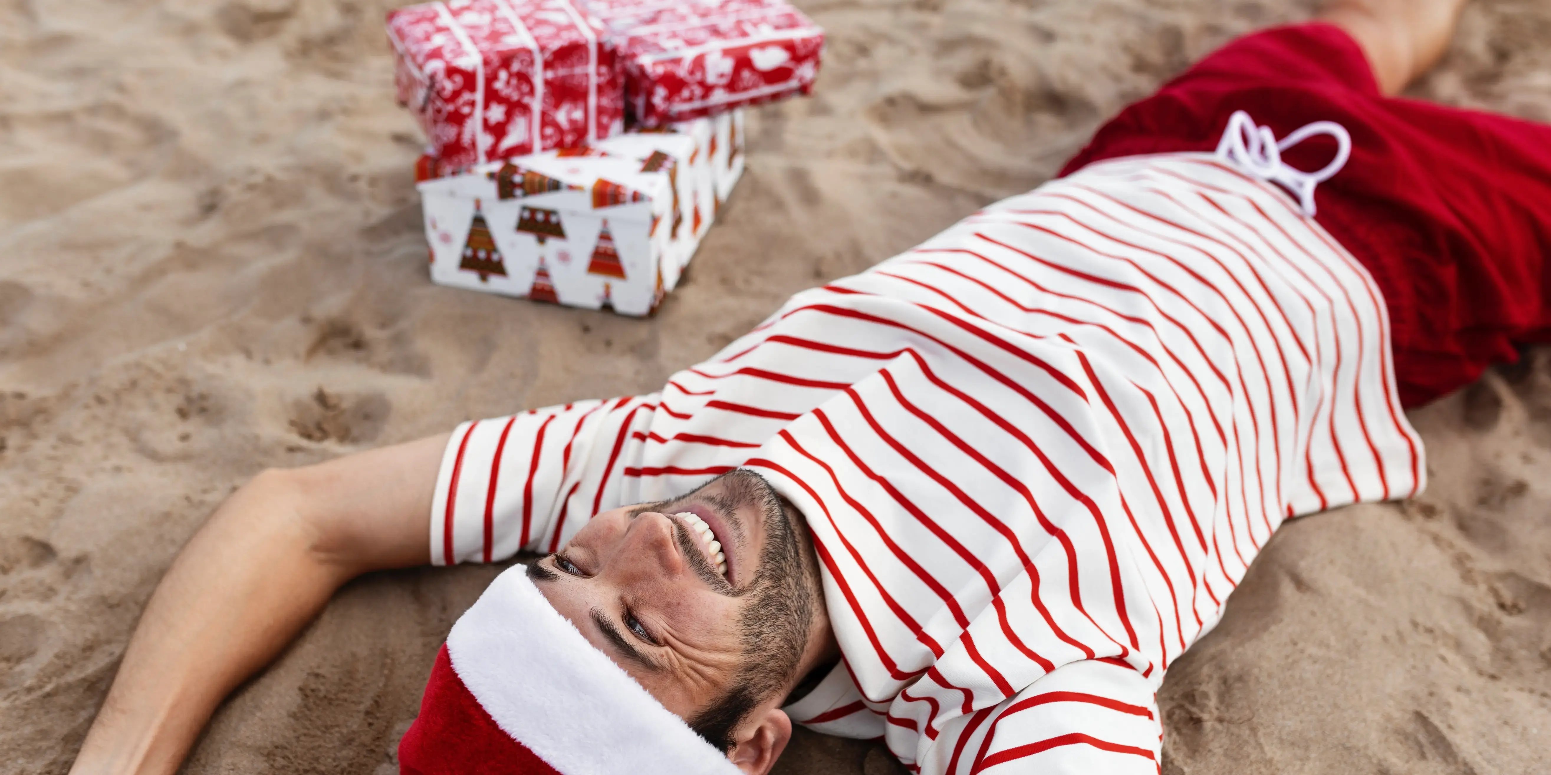 Hombre tirado en la arena con cajas de regalos. Navidad en Quintana Roo