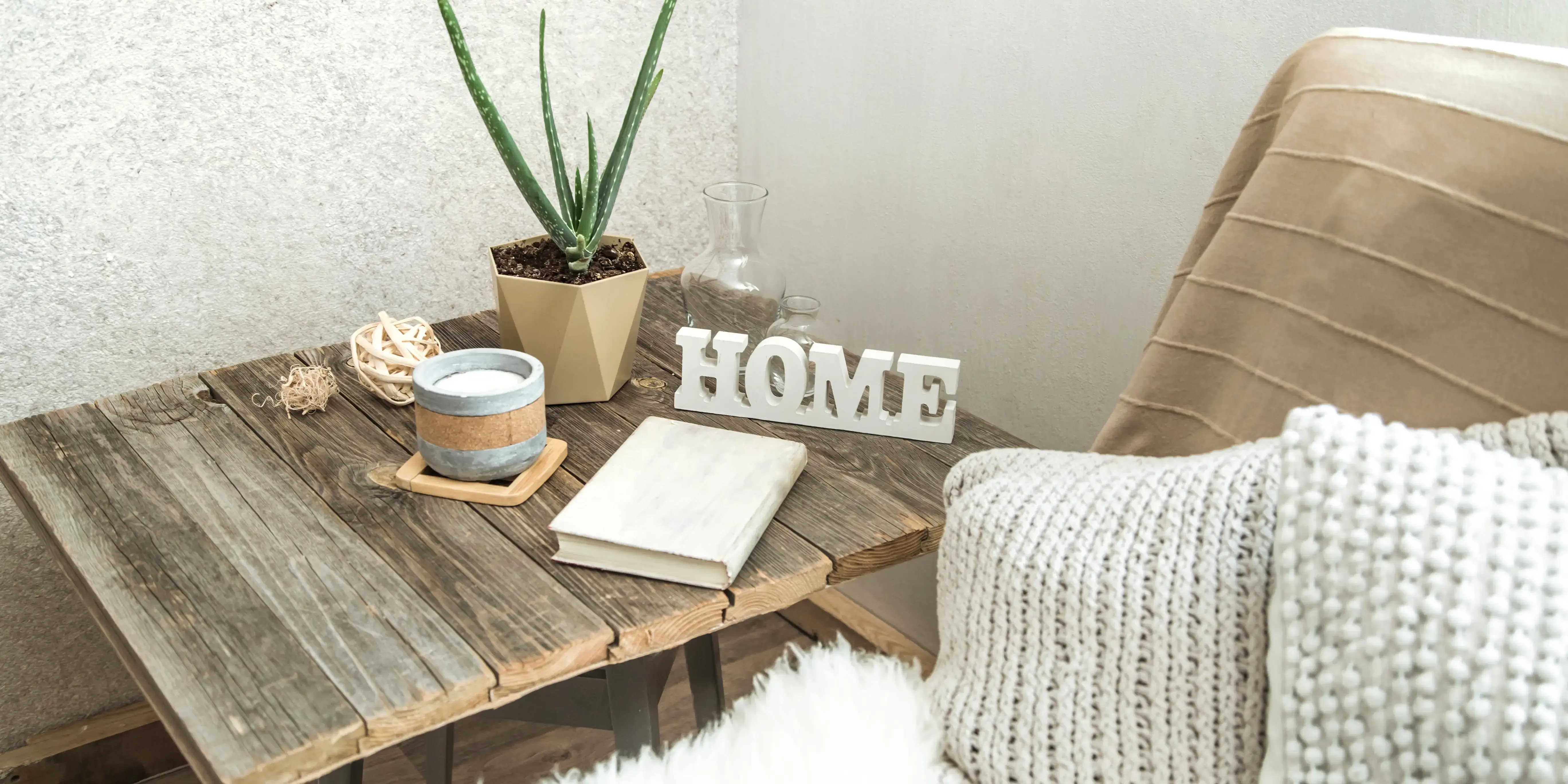 Mesa de madera con una maceta y sillón con manta. Estilo orgánico