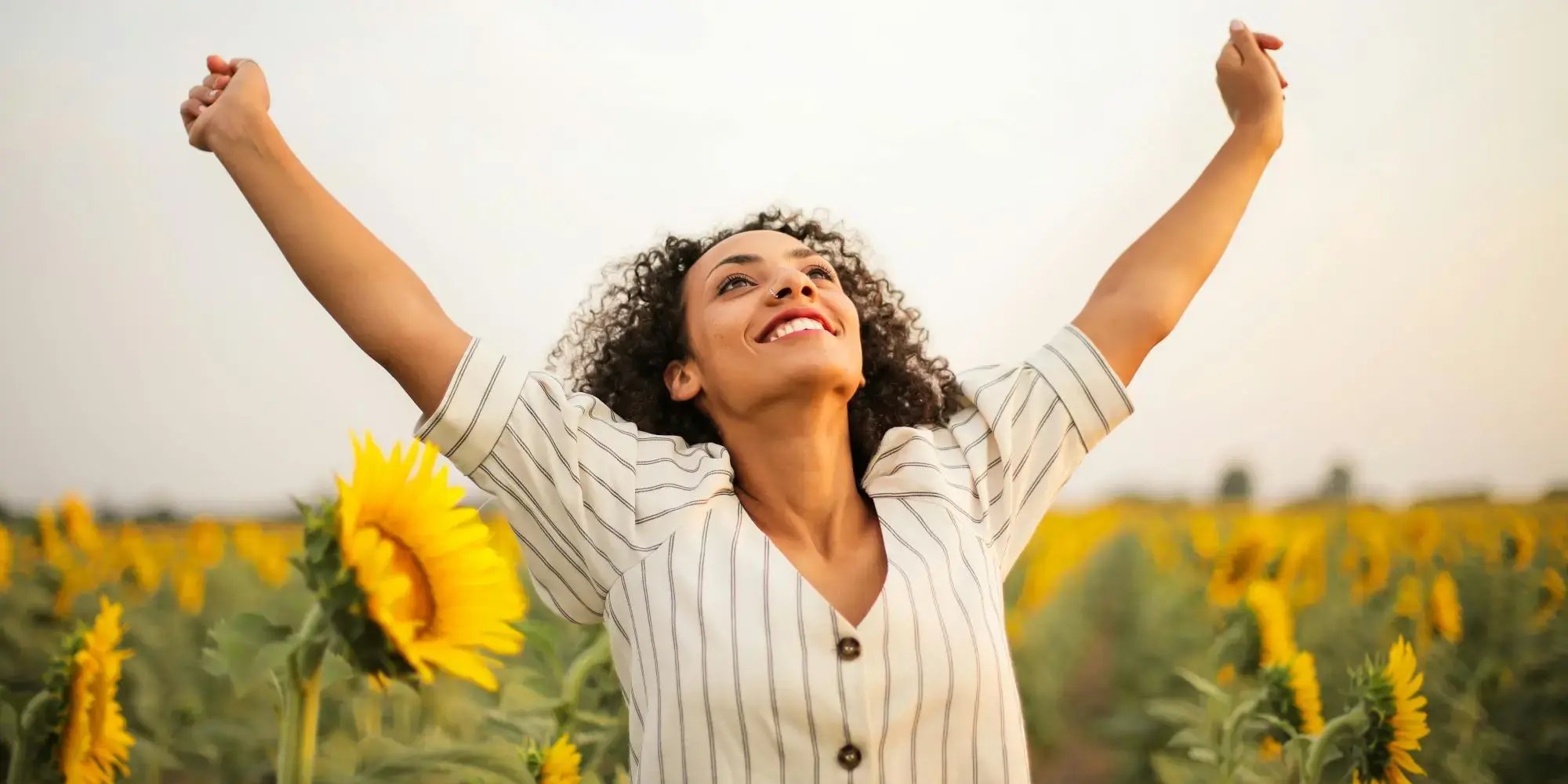 Mujer estira sus brazos en un campo de girasoles para disfrutar el Yellow Day.