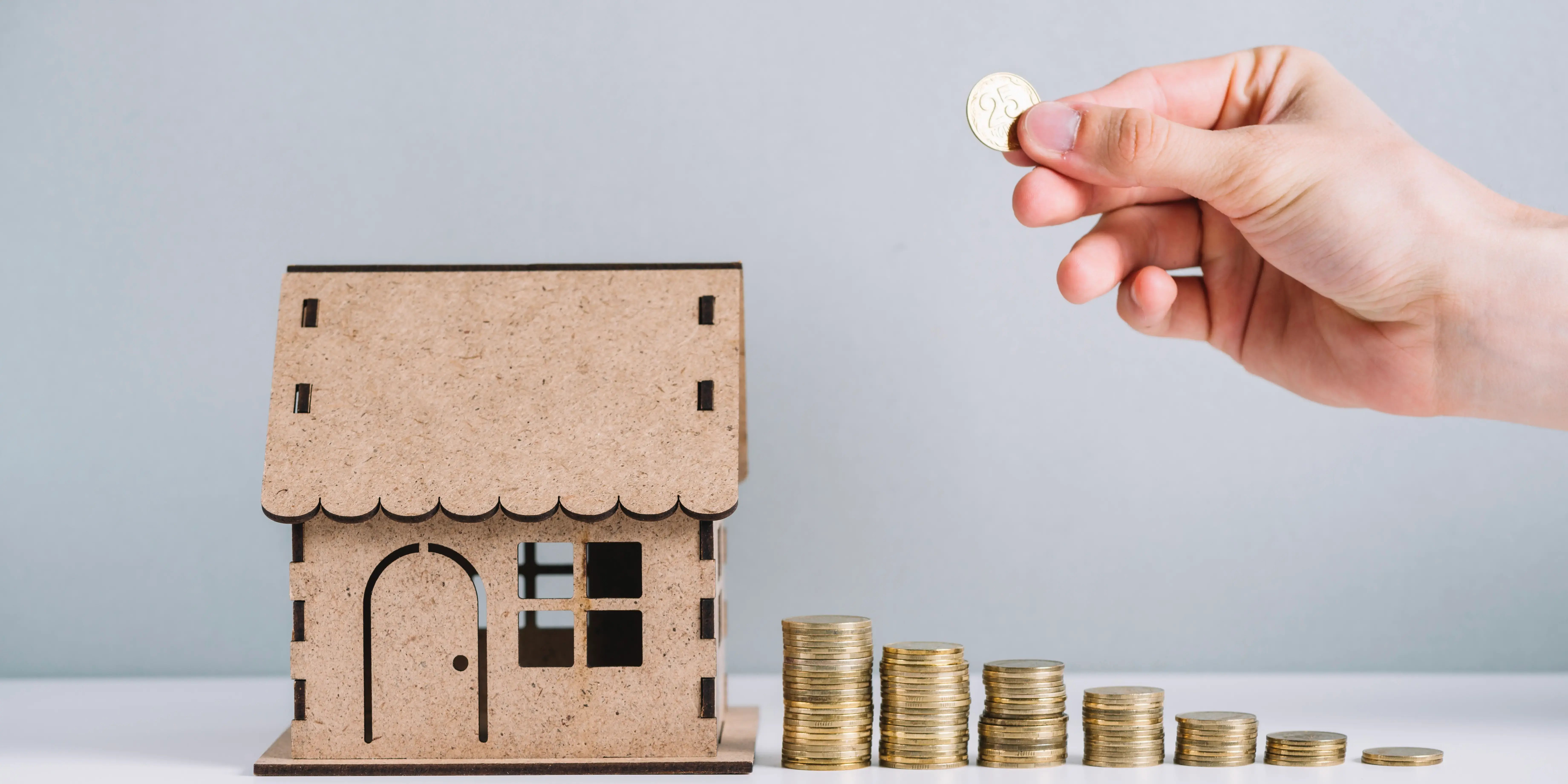 Persona sosteniendo una moneda y pequeñas torres de monedas con una casa de madera. Invertir en bienes raíces