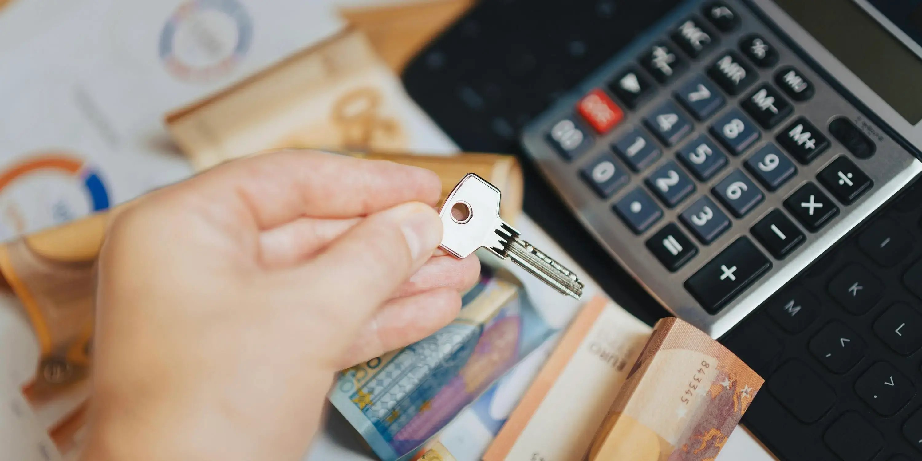 Manos sosteniendo unas llaves y al fondo dinero y una calculadora. Listo para comprar una casa