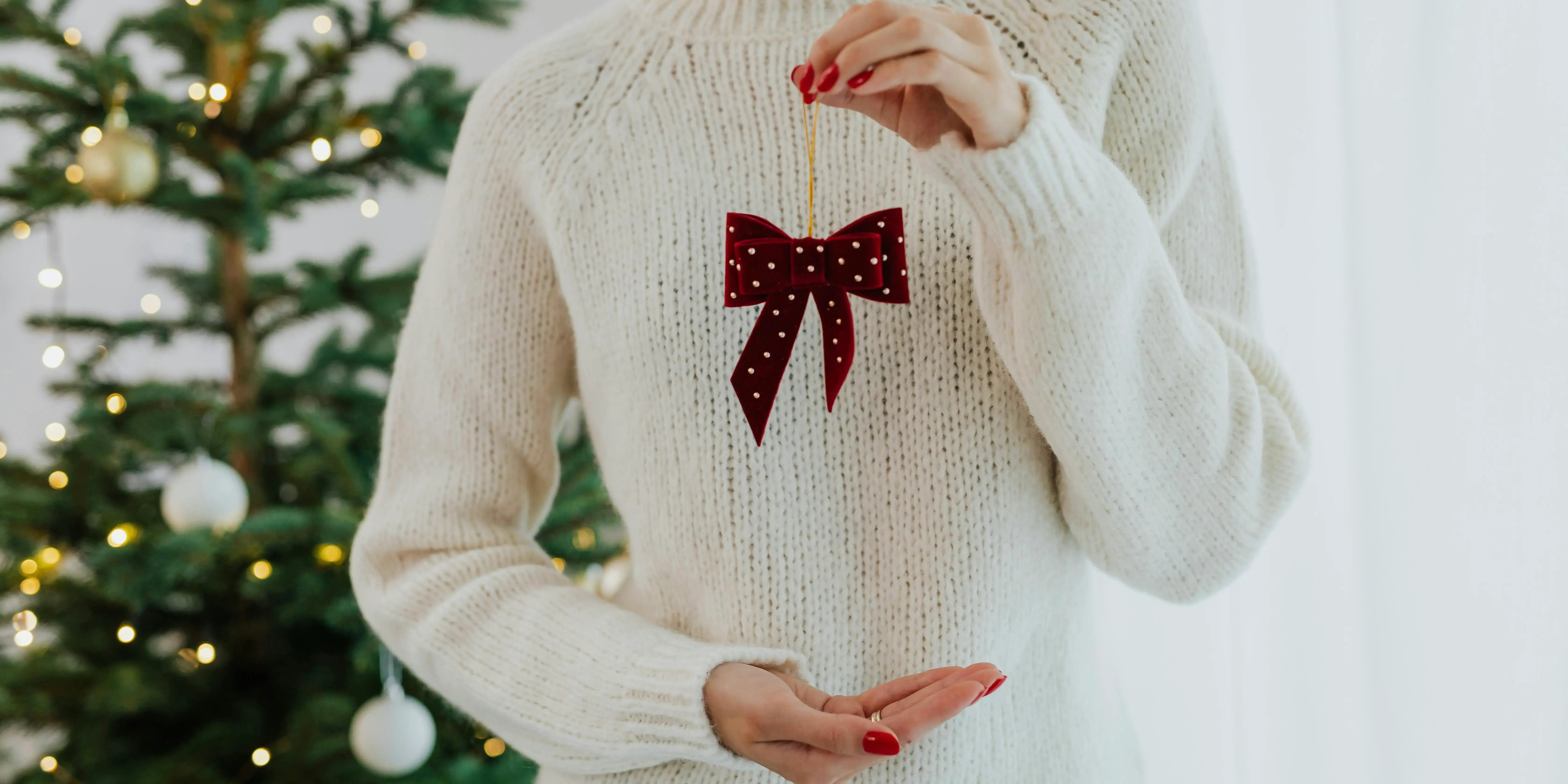 Mujer sosteniendo adorno con árbol de navidad al fondo. Decoración navideña minimalista