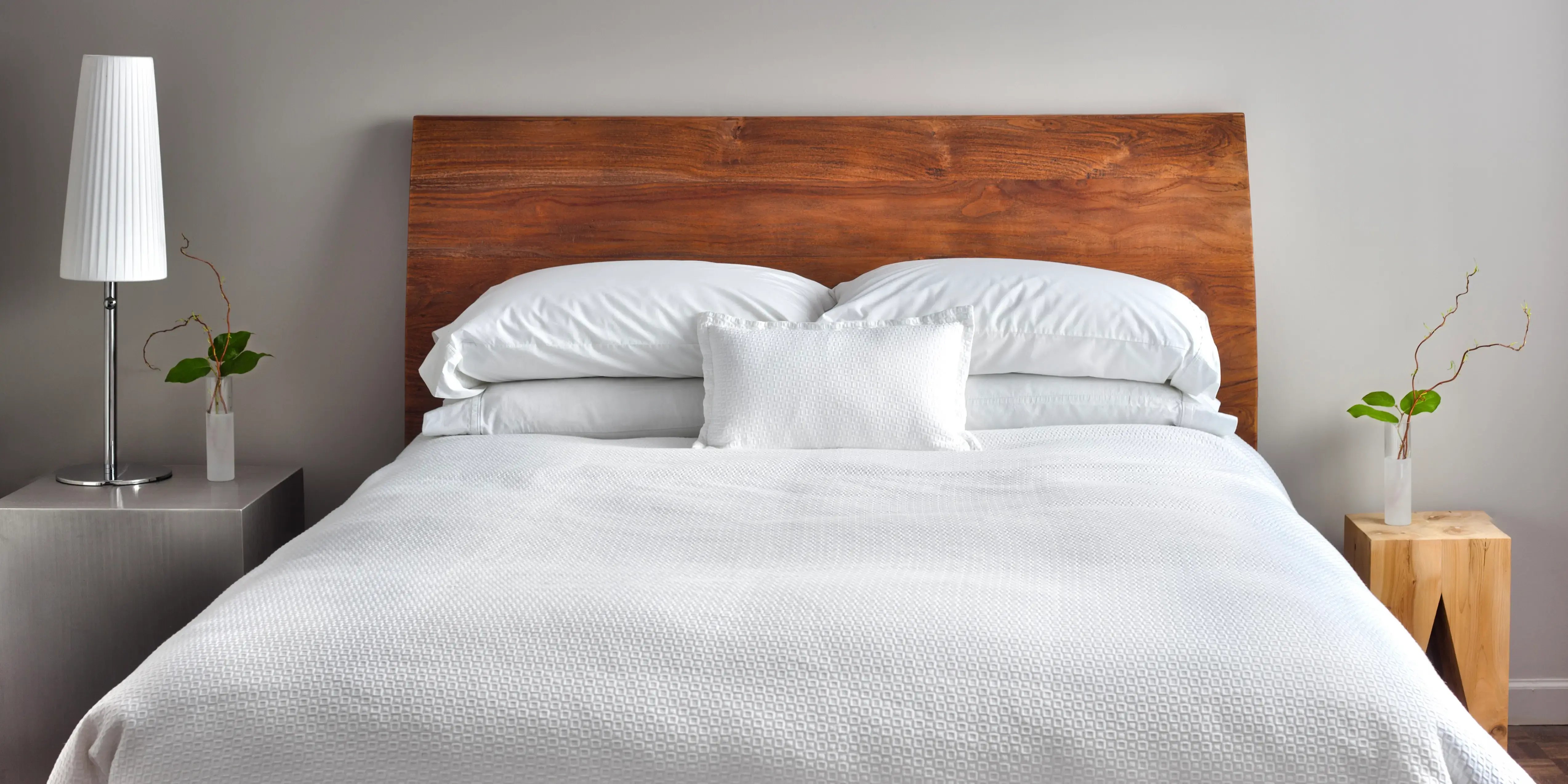 Cama con almohadas y colcha blanca, cabecera de madera y pared gris. Decoración minimalista en la recámara