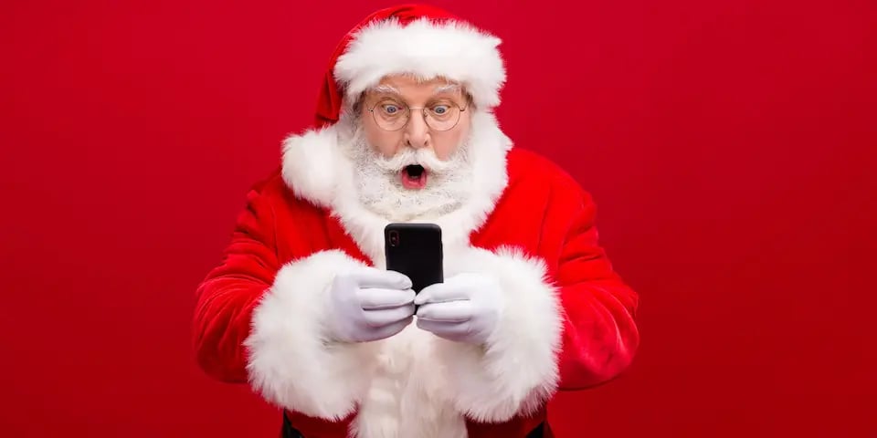 Santa Claus está viendo su celular con sorpresa. El fondo es rojo.
