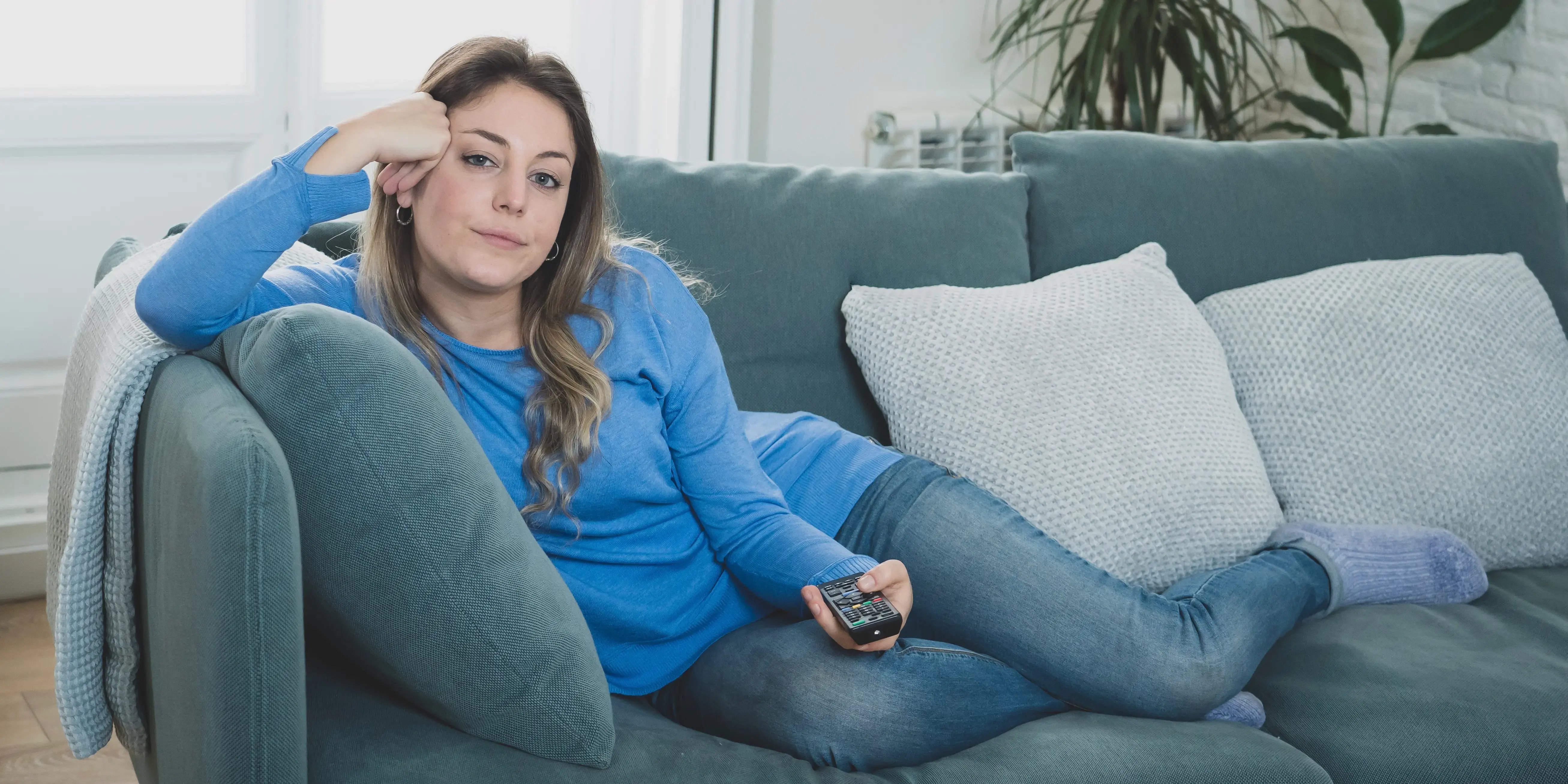 mujer acostada en el sillón con control remoto. ¿Qué es el sedentarismo?