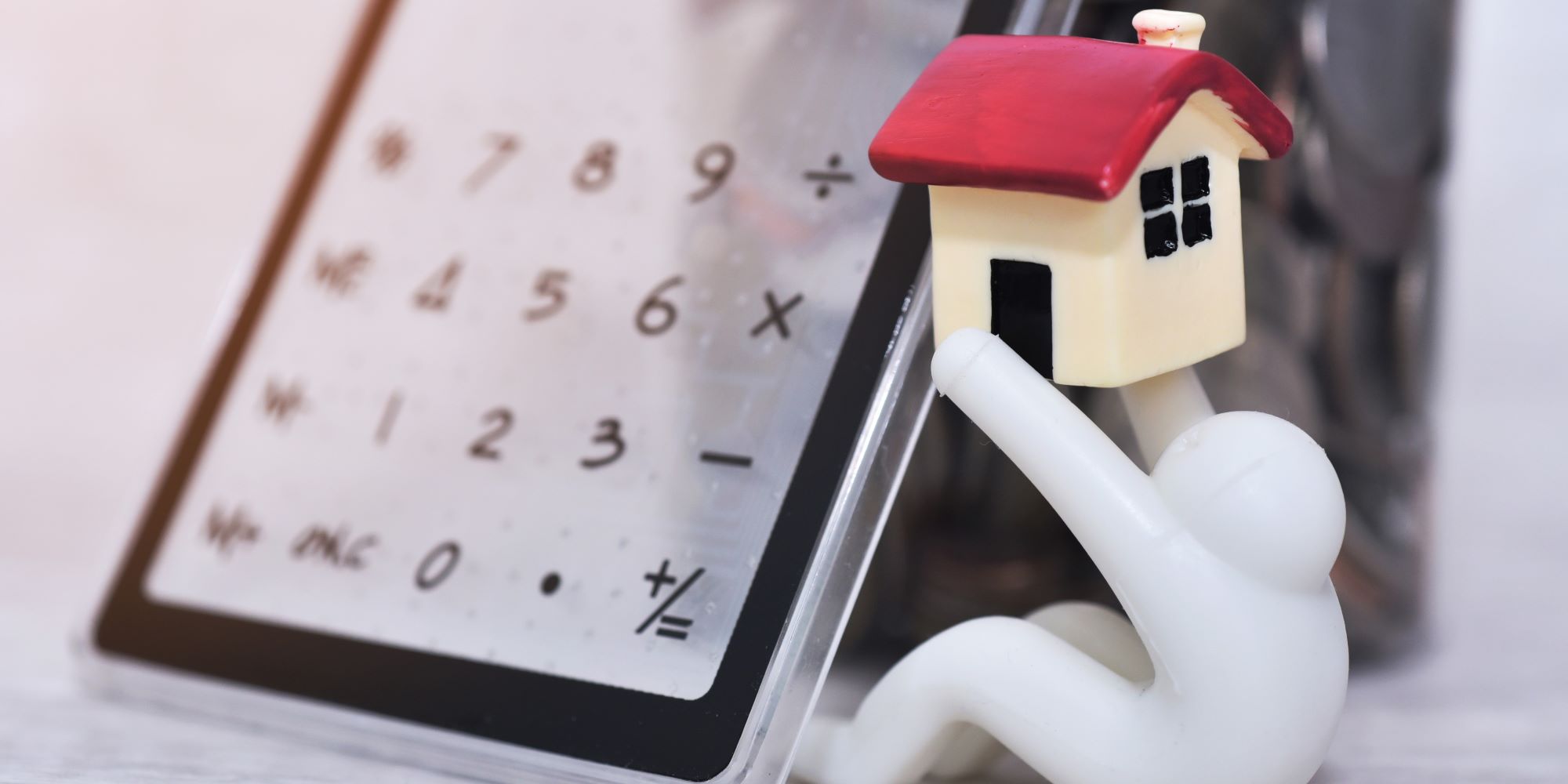 Muñequito sostiene una casita de juguete, y tiene una calculadora al lado. Representa el cálculo de plusvalía de una casa.