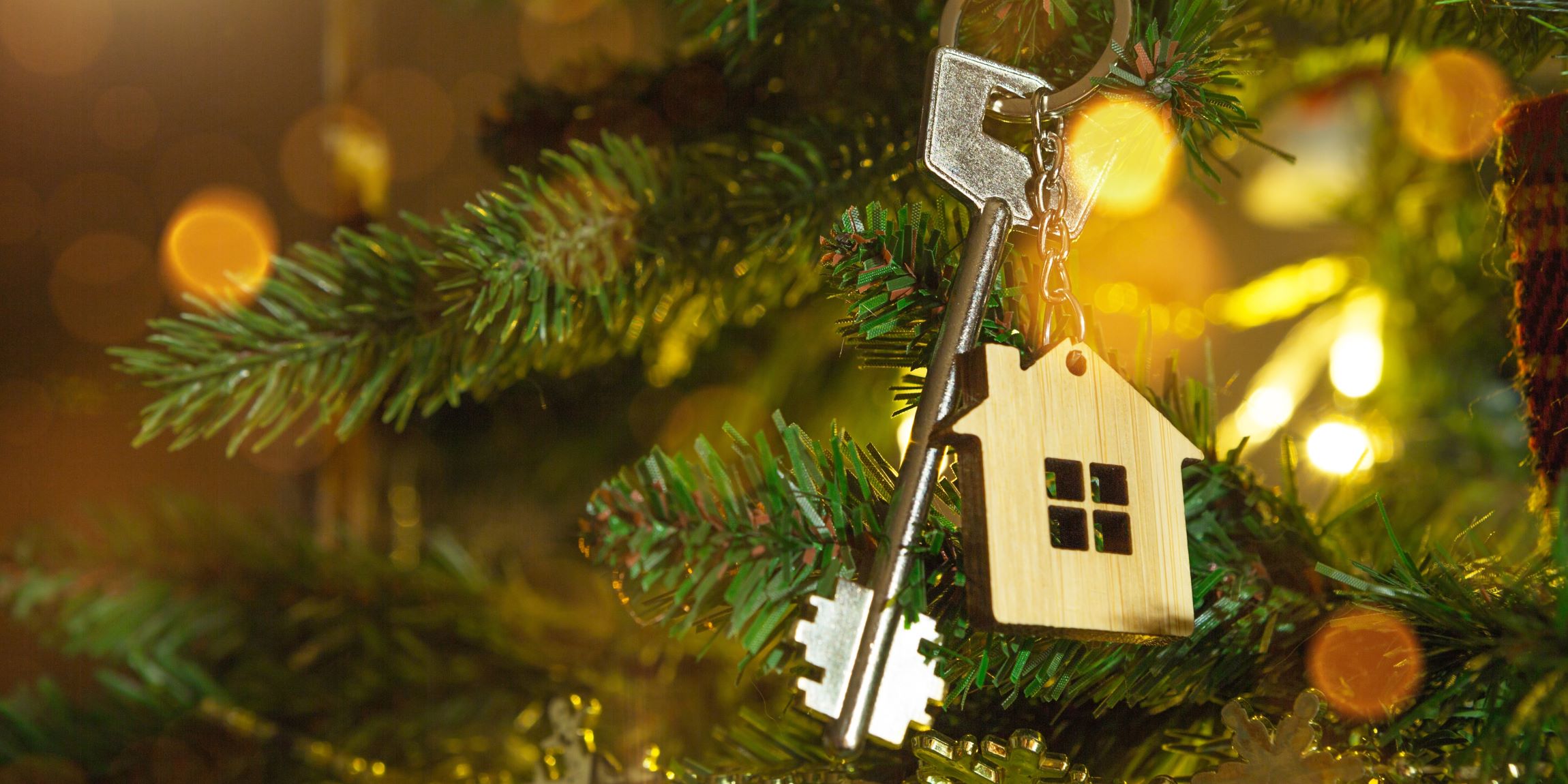 Un árbol de navidad, tiene entre sus adornos una llave con una casita de llavero.