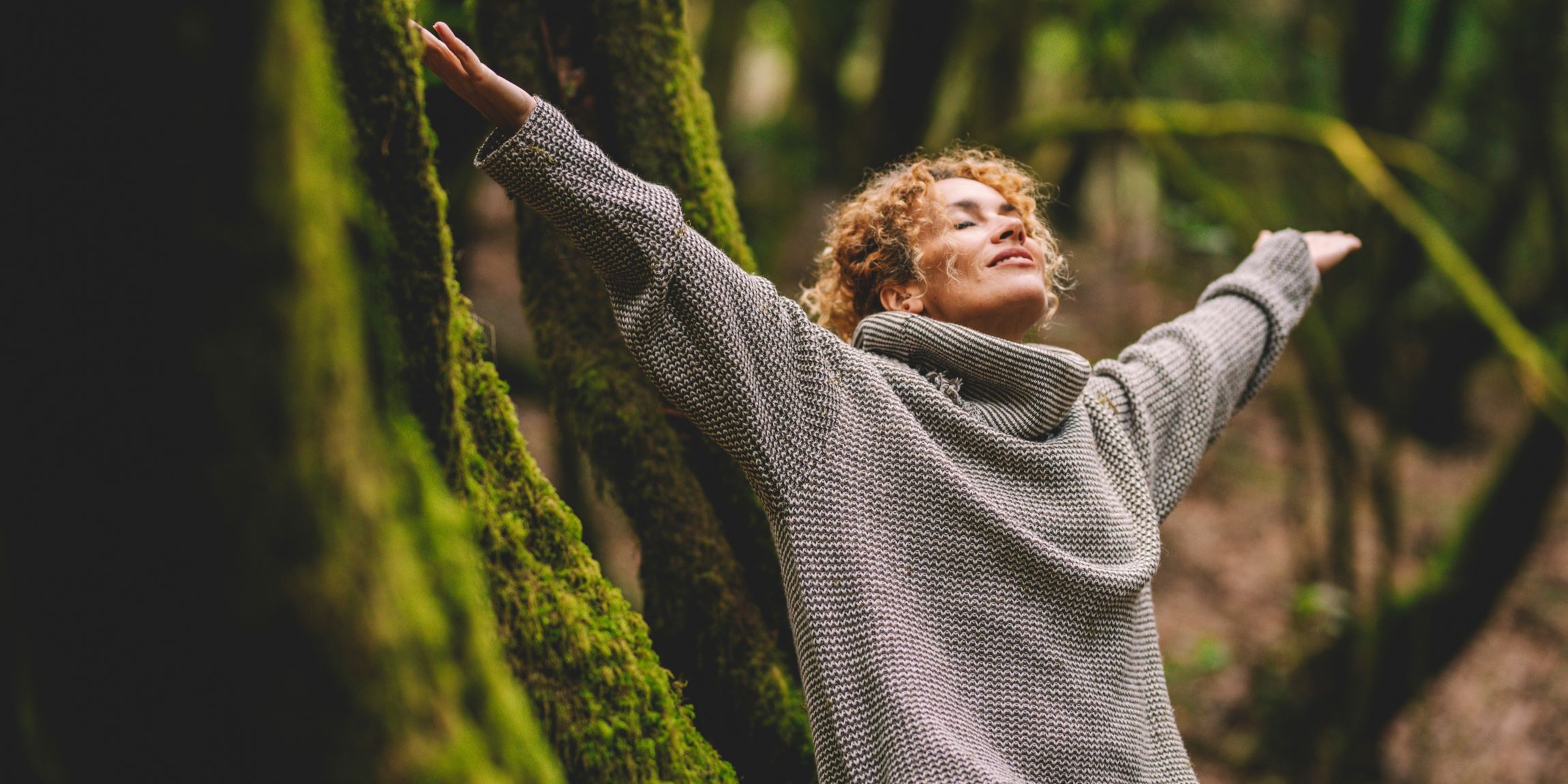 Una mujer feliz en medio del bosque, con los brazos extendidos, y sintiendo la naturaleza. 