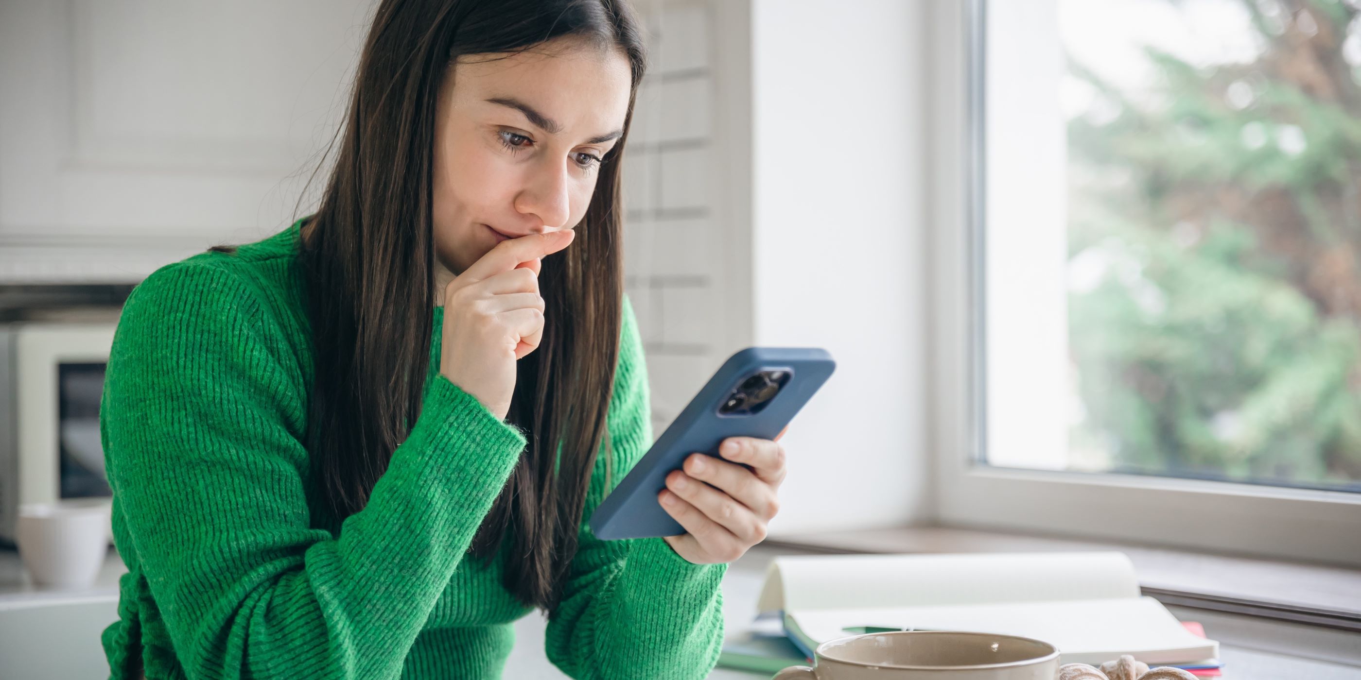 Mujer está observando atentamente su celular. Está pensando en su siguiente compra y si es una buena opción.