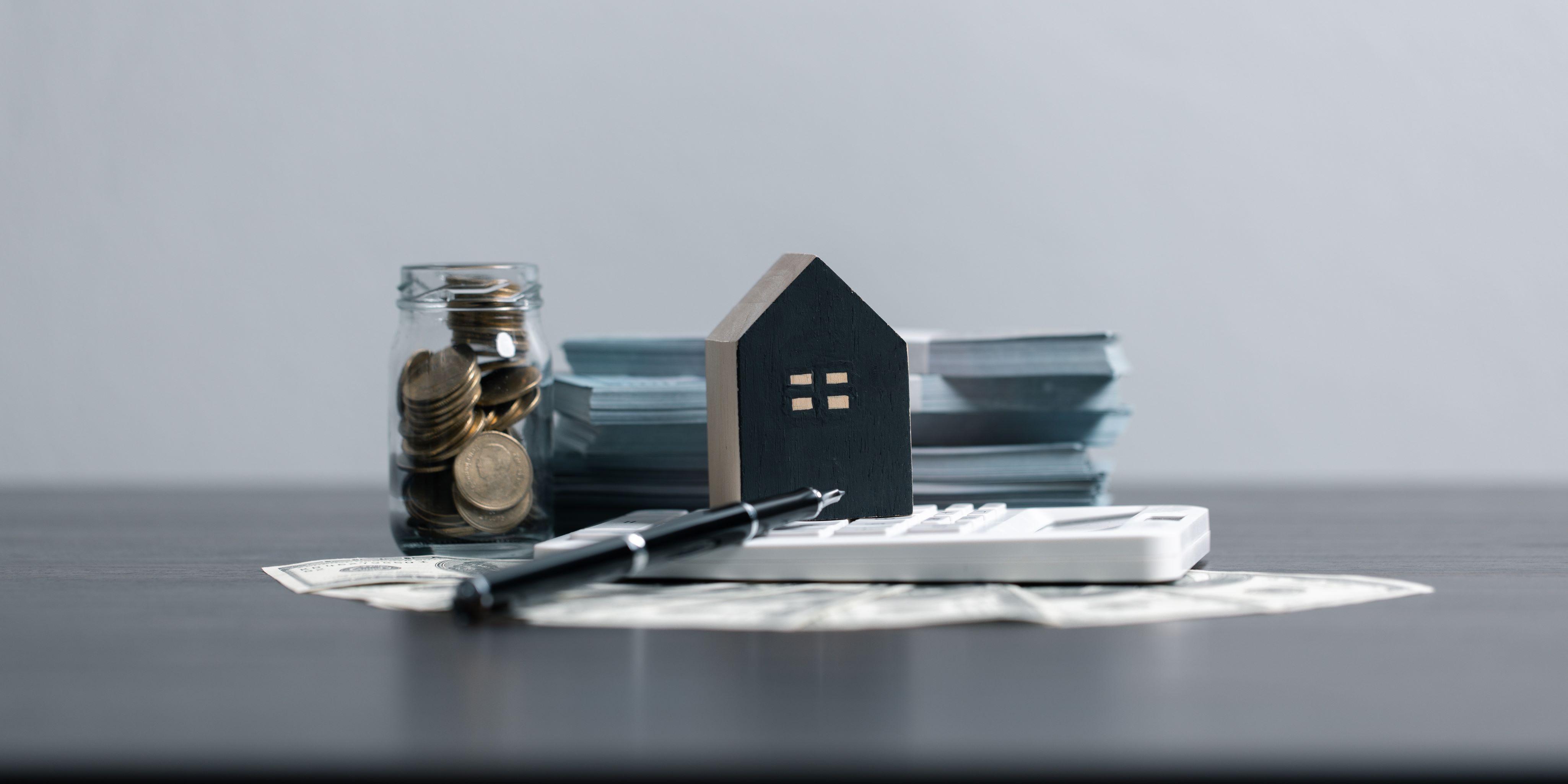 Papeles de préstamo hipotecario, un frasco de dinero y una pequeña casita pintada de negro en la fachada. Calculadora, y papeles.