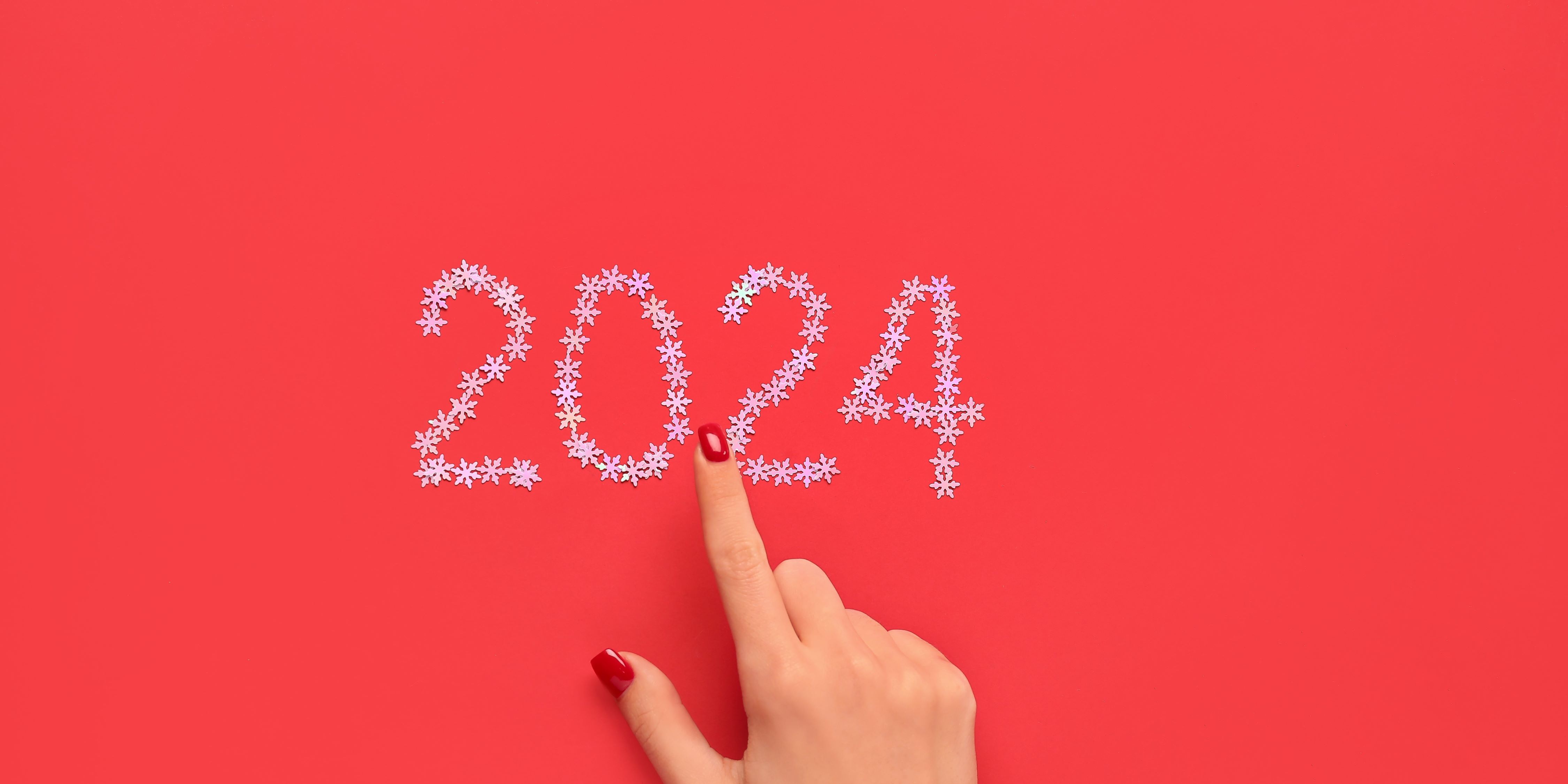 Propósitos de año 2024. Mujer apunta con su mano al 2024 dibujado ocn estrellitas plateadas en un fondo rojo. 