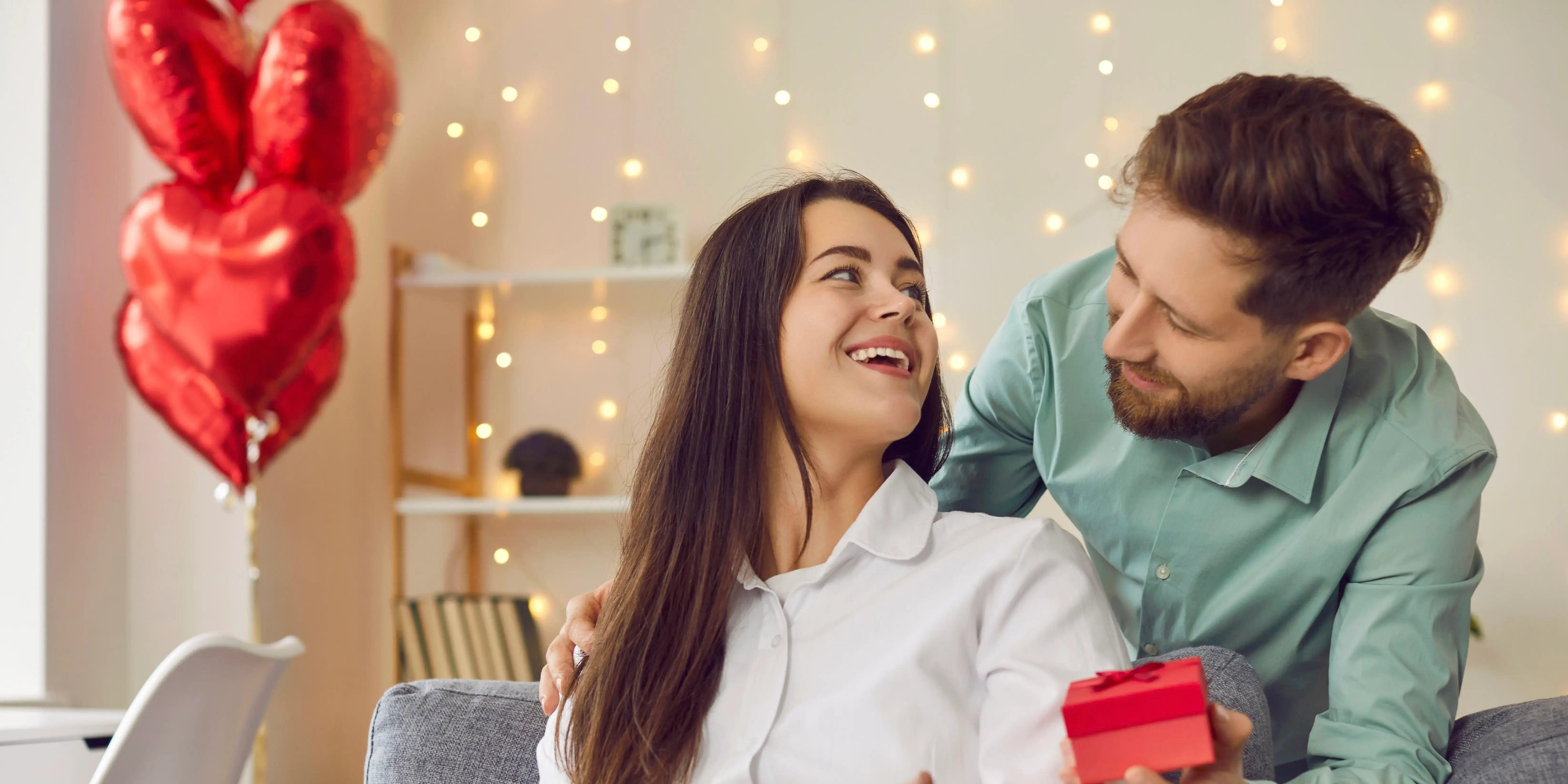 Sala con globos de corazón y hombre con caja de regalo. San Valentín inolvidable en tu hogar