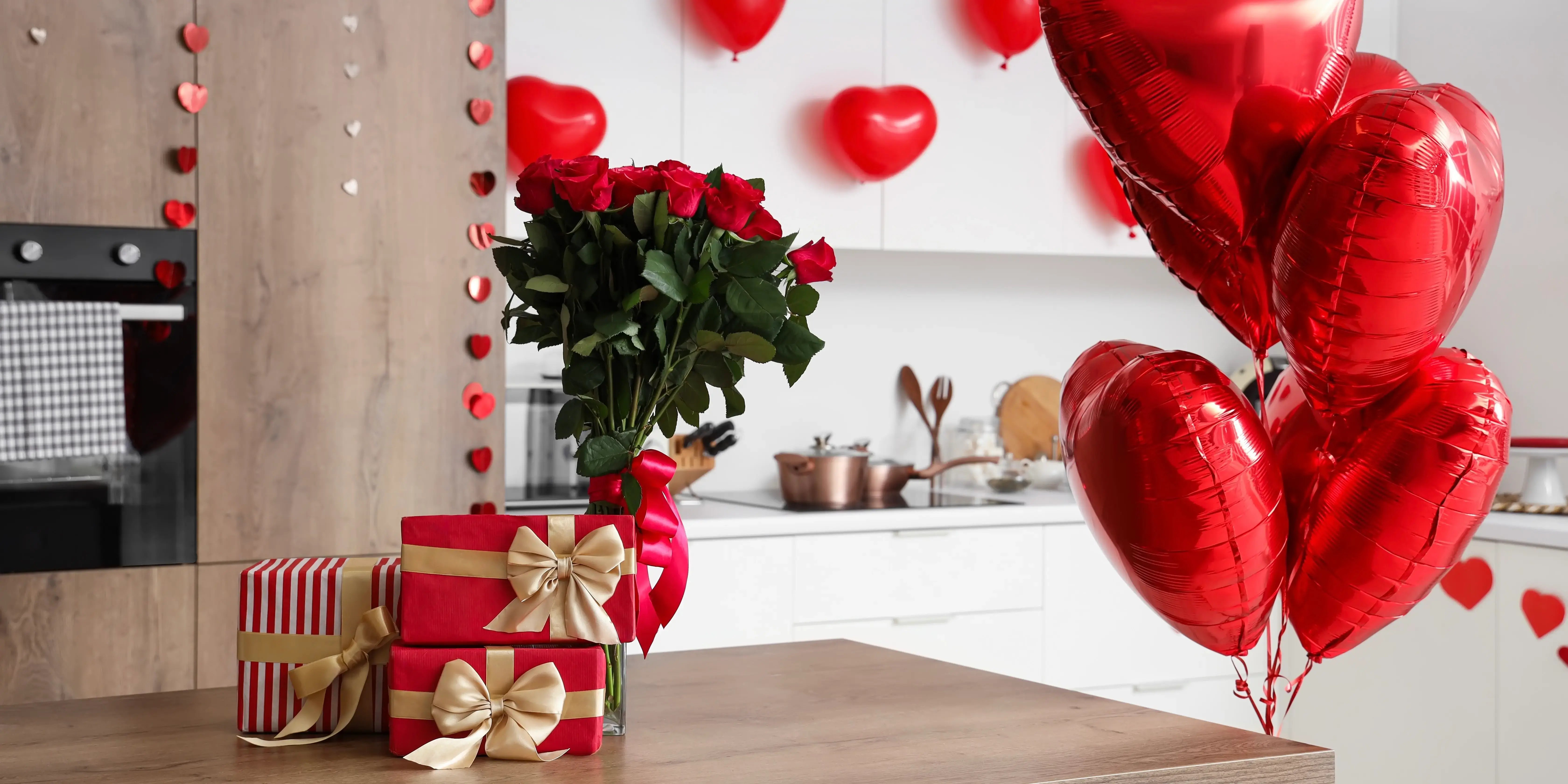 Cocina con cajas de regalos, ramo de flores y globos en forma de corazón. Decorar departamento San Valentín