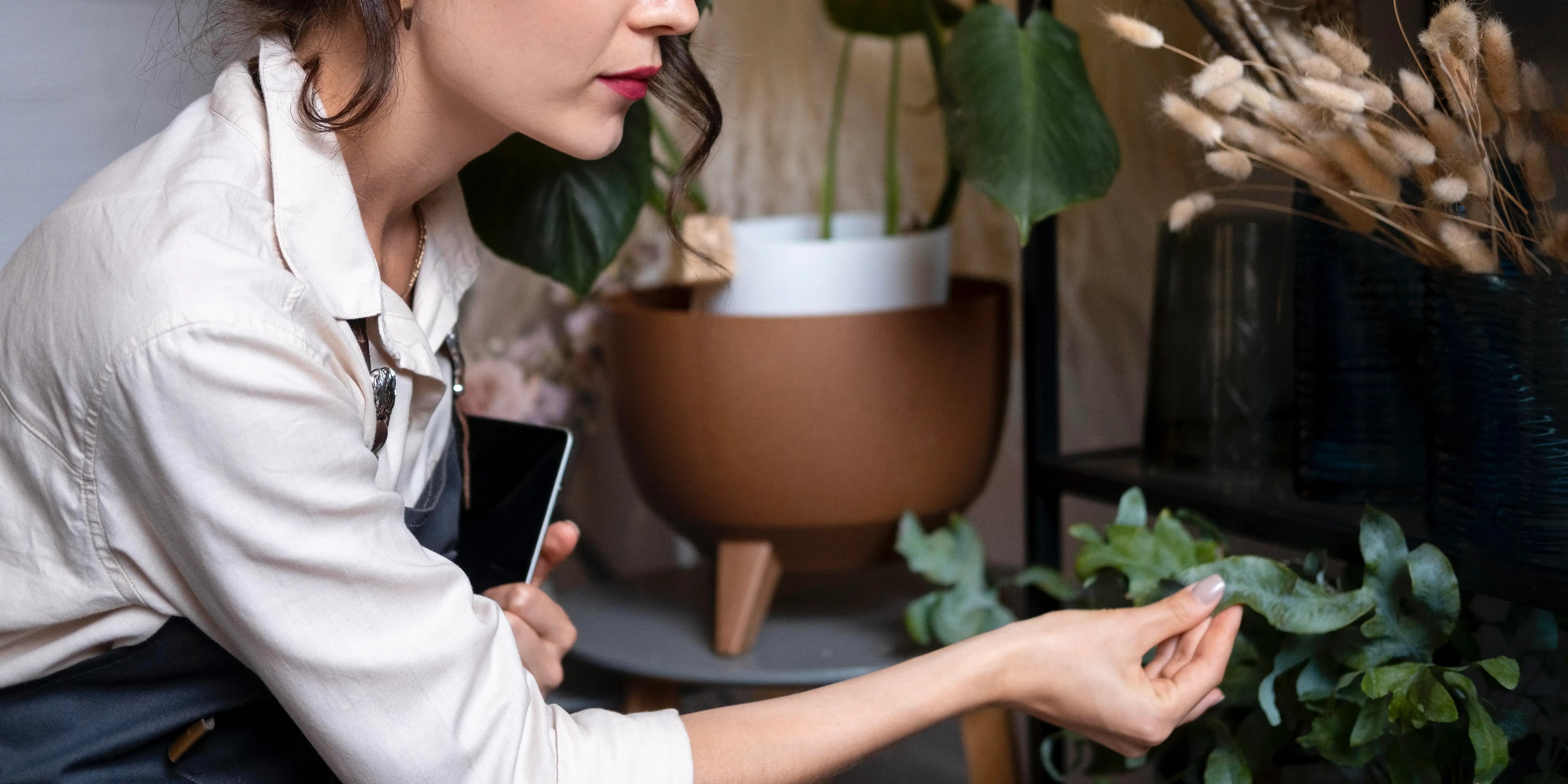 Mujer agarrando una planta y una maceta al fondo.Diseño biofílico