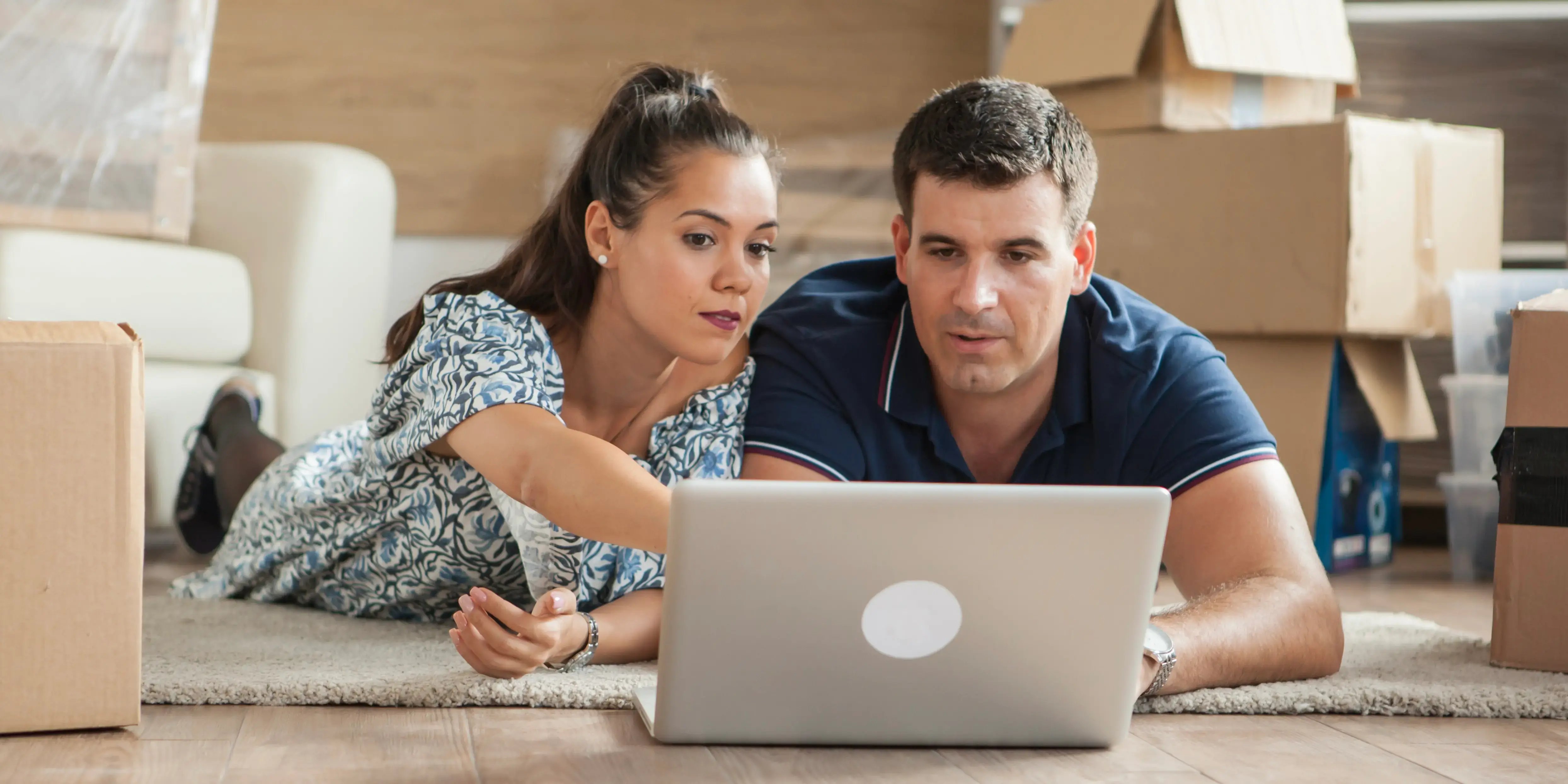 Hombre y mujer con cajas de mudanza viendo una computadora. Desarrollo inmobiliario para vivir