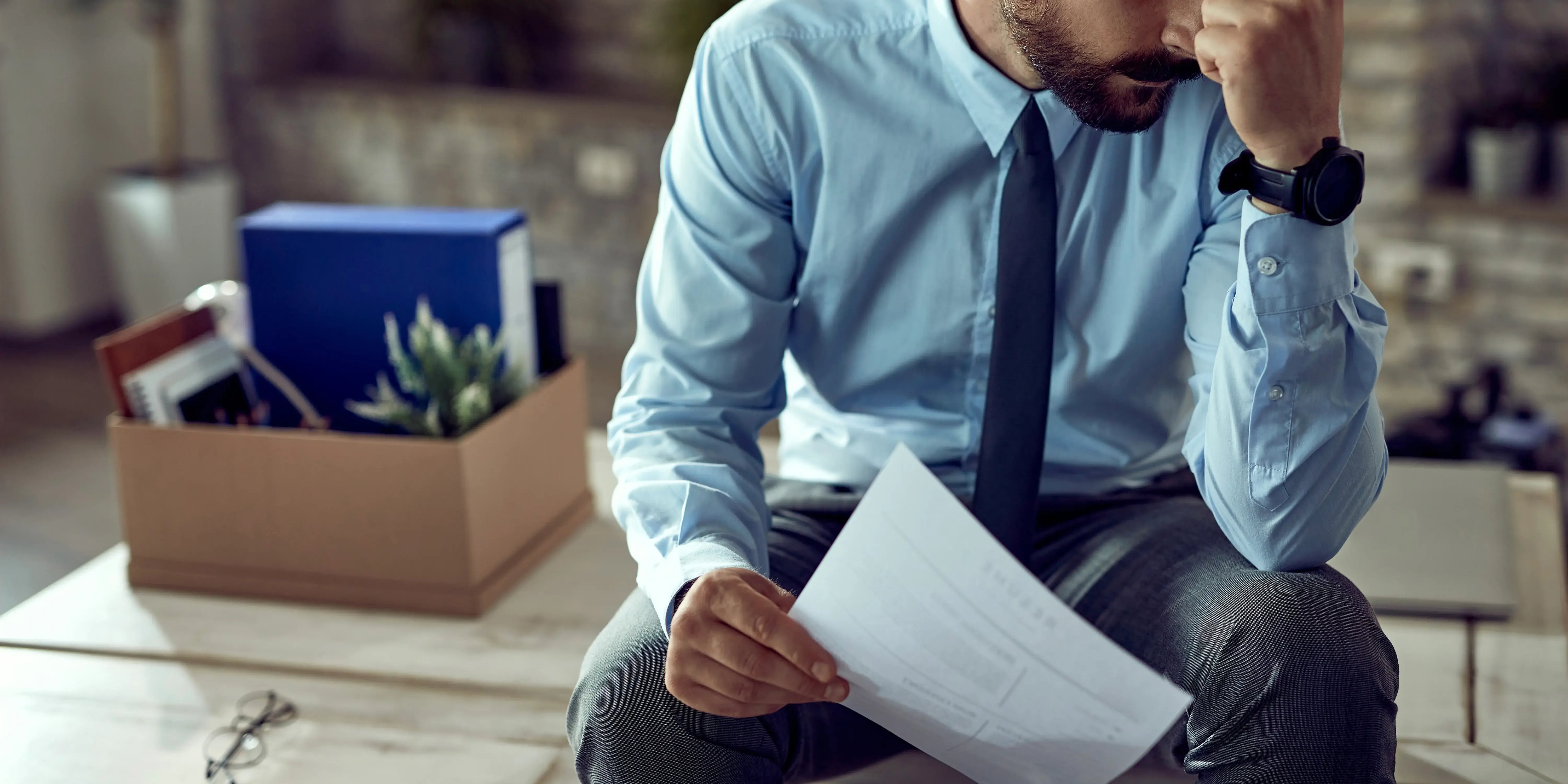Hombre sosteniendo un papel y caja con cosas de la oficina Retiro por desempleo